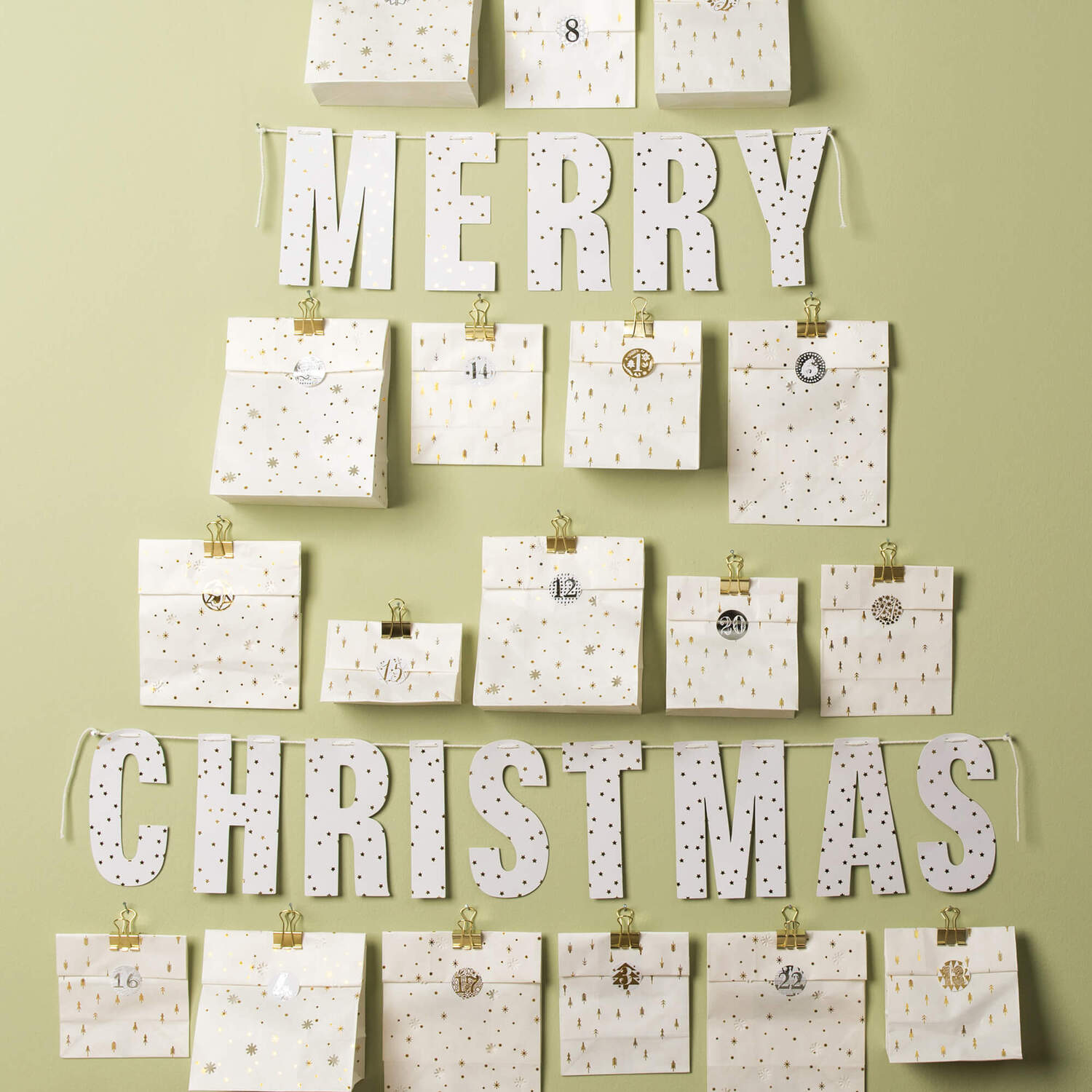 Bastelanleitung Adventskalender aus Lichtertüten: Ein DIY-Kalender in Form eines Weihnachtsbaums mit nummerierten Tüten und goldenen Clips.