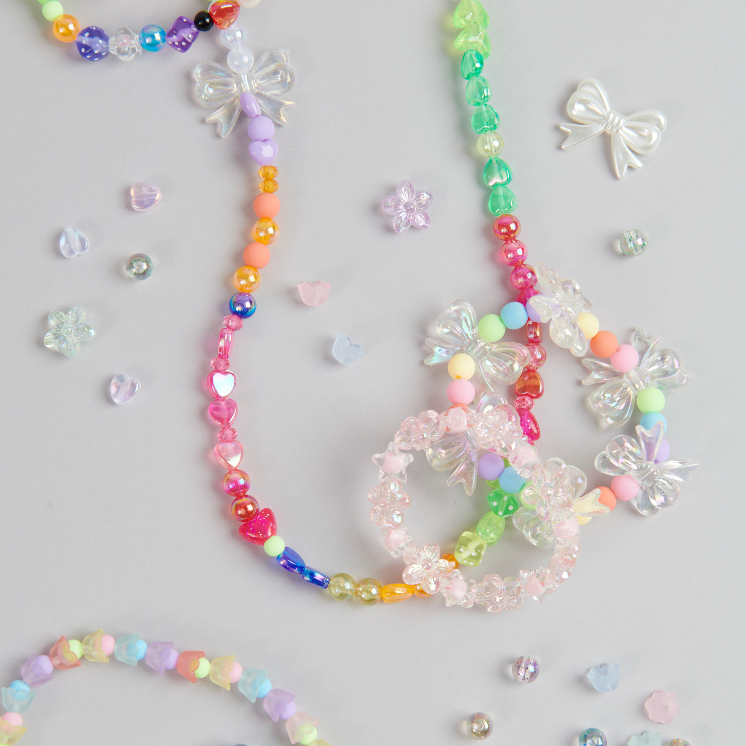 itoshii Herzperlen Regenbogen: Bunte Perlenketten mit Herz- und Schleifenperlen auf grauem Hintergrund.