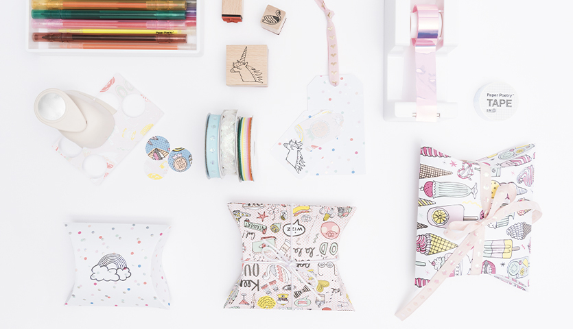 Bastelanleitung Geschenkschachteln: Kreatives Set mit buntem Papier, Stempeln und Bändern für individuelle Geschenkverpackungen.