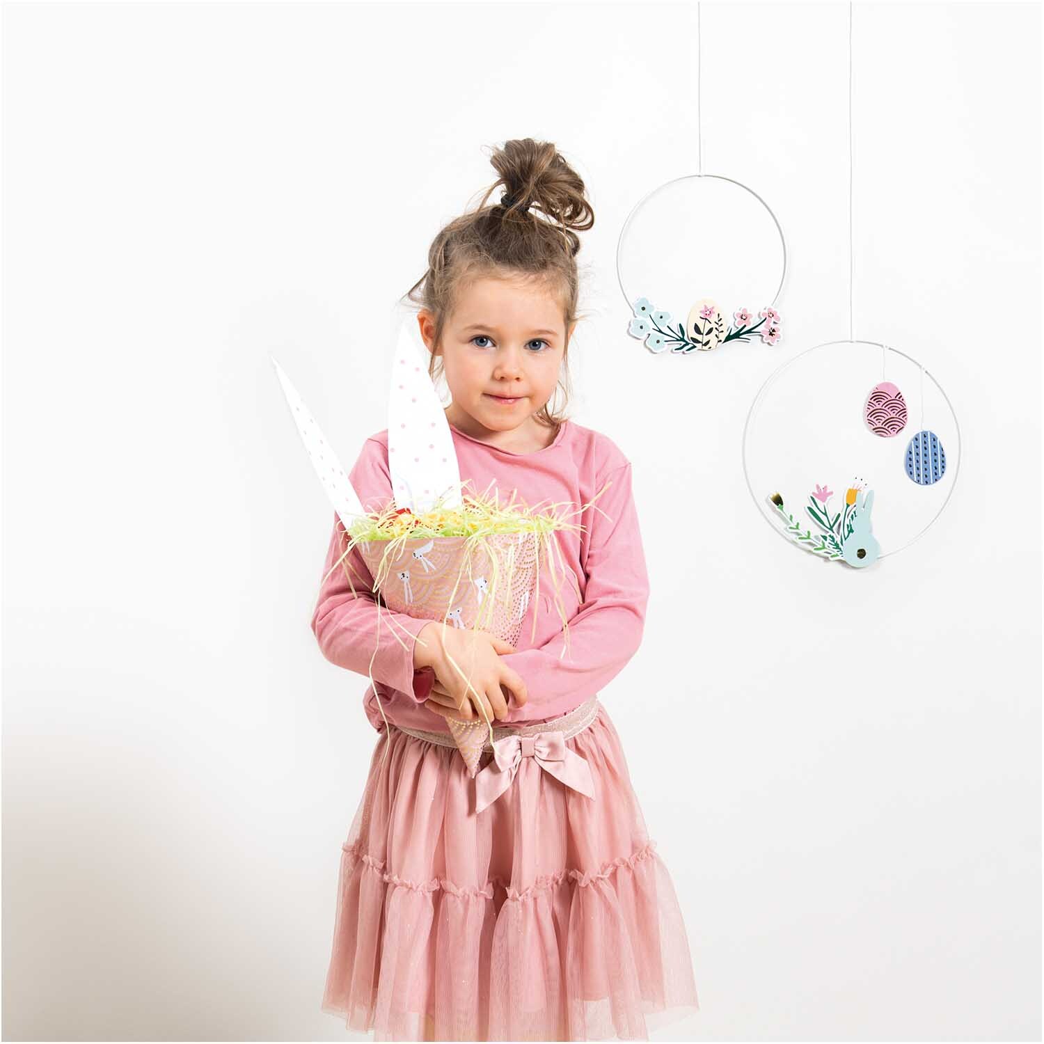 Paper Poetry Motivkarton Bunny Hop zeigt ein Mädchen in rosa Kleid mit Osterdekoration.