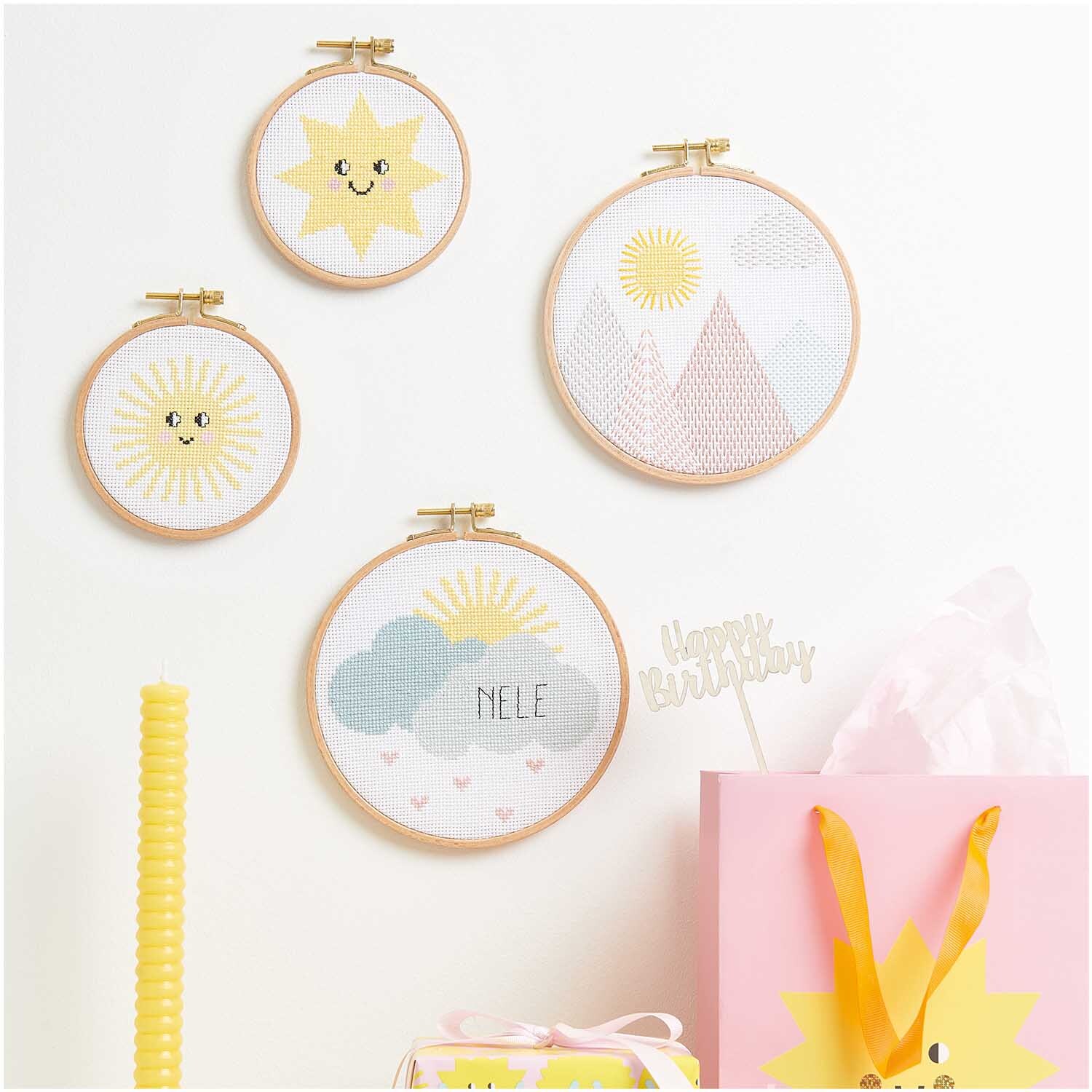 Stickpackung Happy Sun: Vier Stickrahmen mit Sonnen- und Bergmotiven, dekorativ arrangiert.