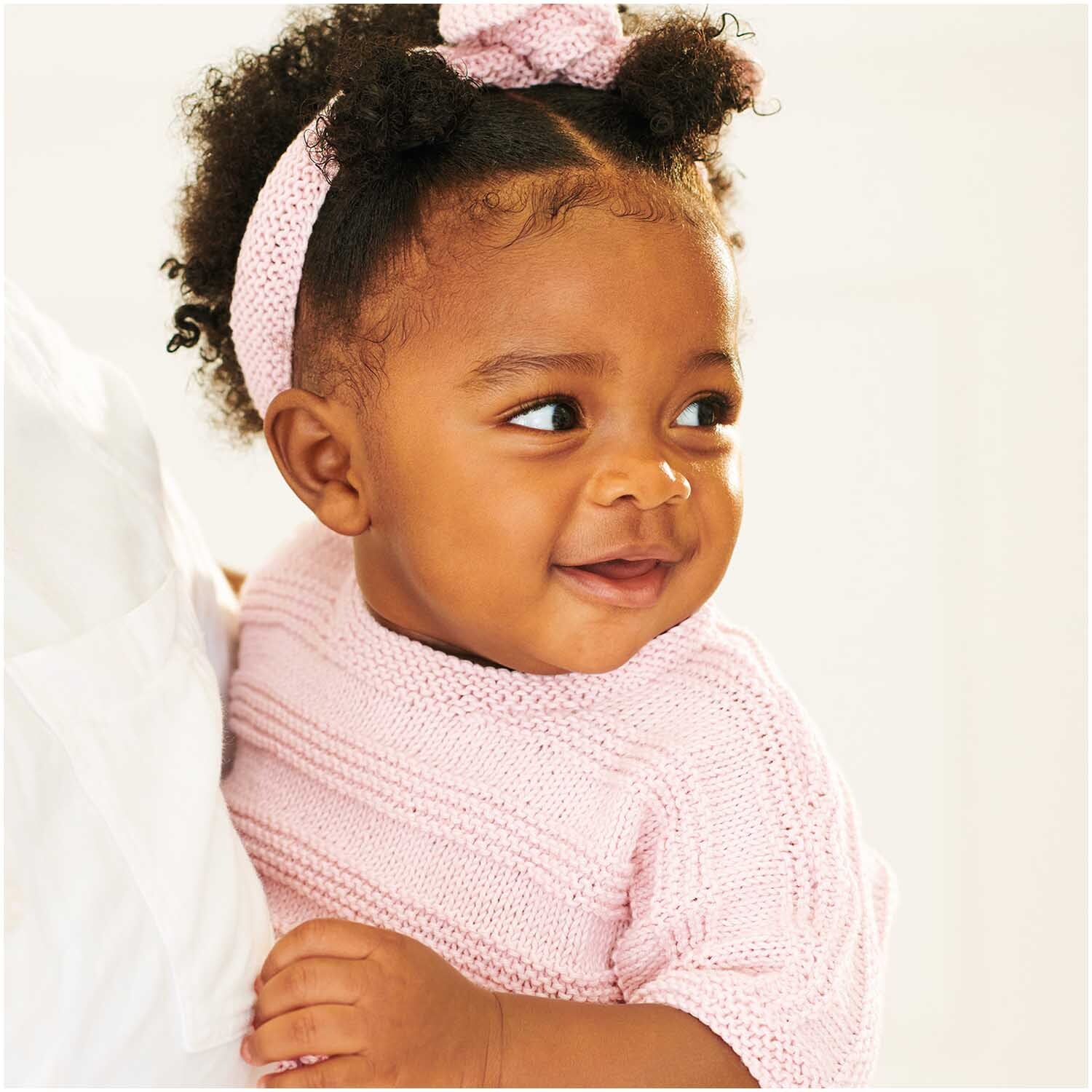 Baby Organic Cotton: Niedliches Baby in rosa Strickkleidung aus Bio-Baumwolle, lächelnd und glücklich.