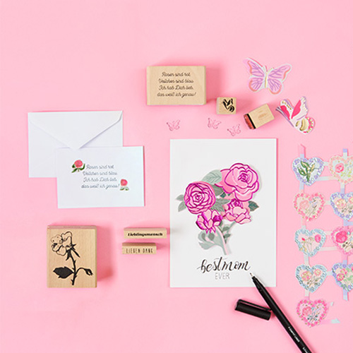 Karten und Umschlag mit pinkem Blumendesign und passenden Stempel und Sticker. Flatlay von Produkten.