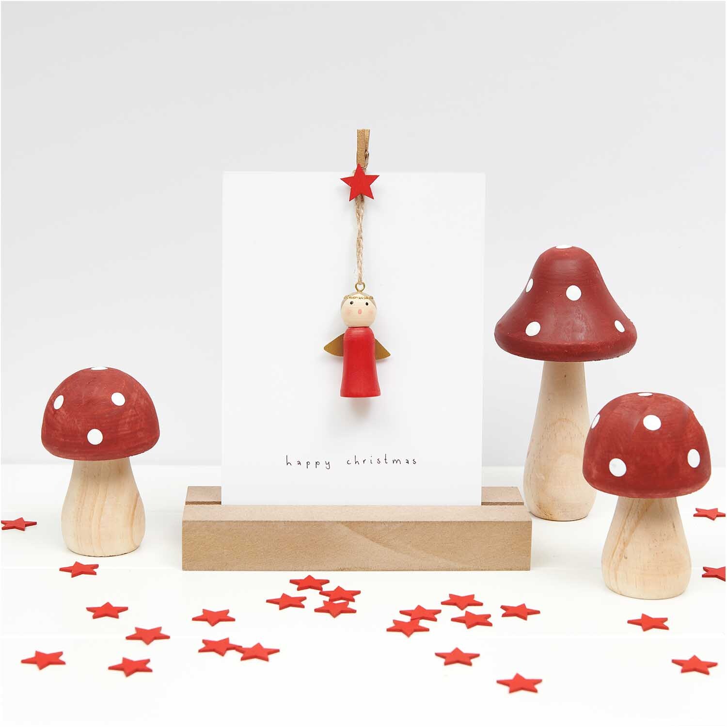 Dekoklammern Stern rot 3cm 8 Stück von Rico Design: Rote Sternklammer hält Karte mit Engel, umgeben von roten Pilzen und Sternen auf weißem Hintergrund.