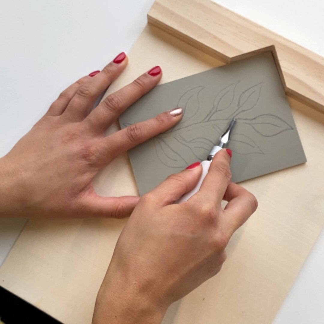 Ricolino Linolschnittwerkzeug zeigt eine Hand beim Schnitzen eines Blattmotivs in eine Linolplatte, gehalten im Ricolino Schnitzblockhalter von Rico Design, 6-teilig.