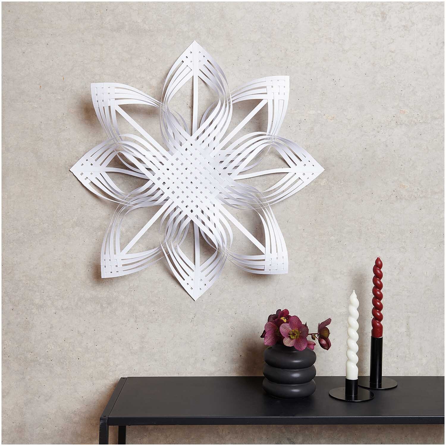 Paper Poetry Web-Stern Größe L von Rico Design an einer Wand, dekoriert mit Kerzen und Blumen.