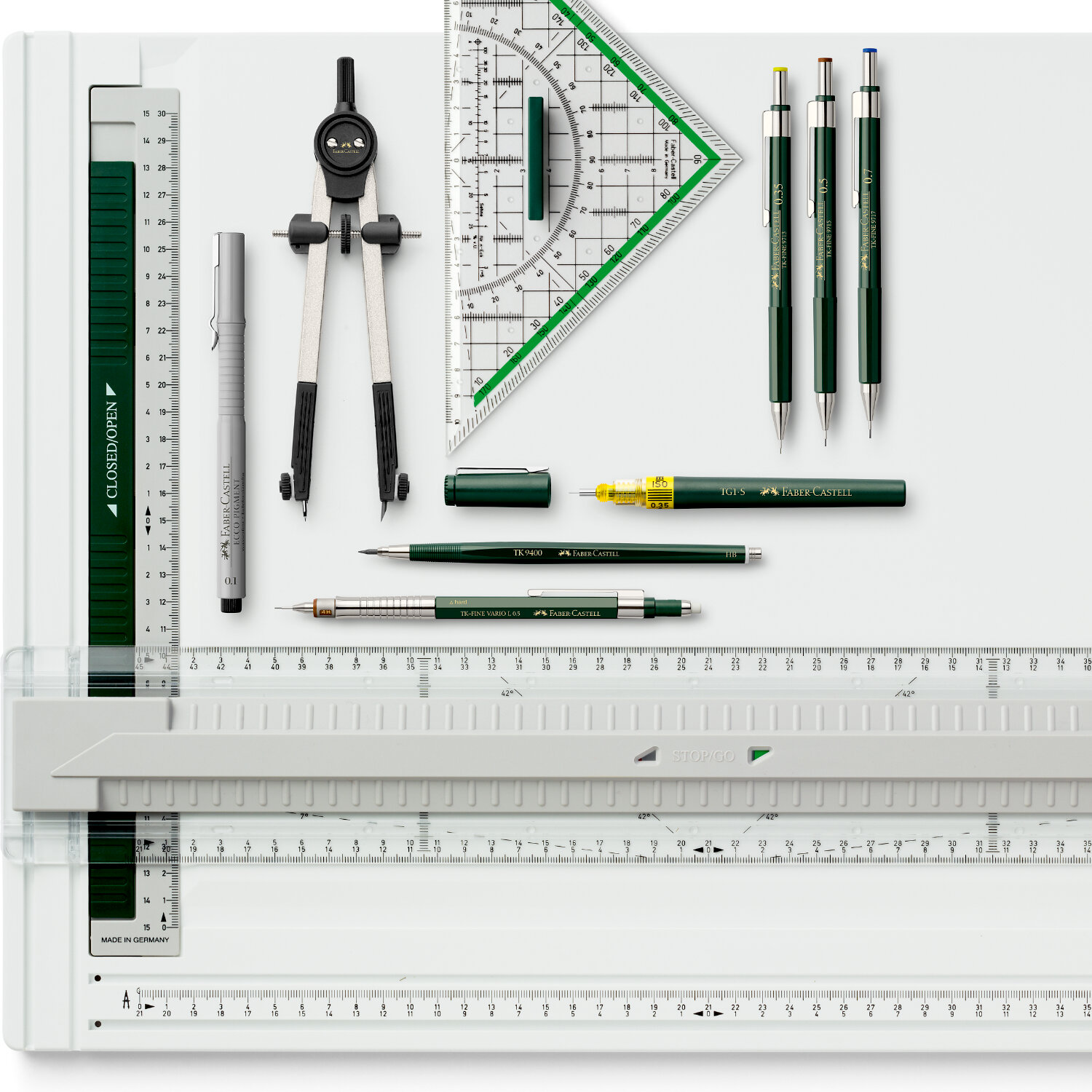 TK 9400 Fallminenstift von Faber Castell neben Zeichenwerkzeugen wie Linealen, einem Zirkel und einem Geodreieck auf einem weißen Hintergrund.