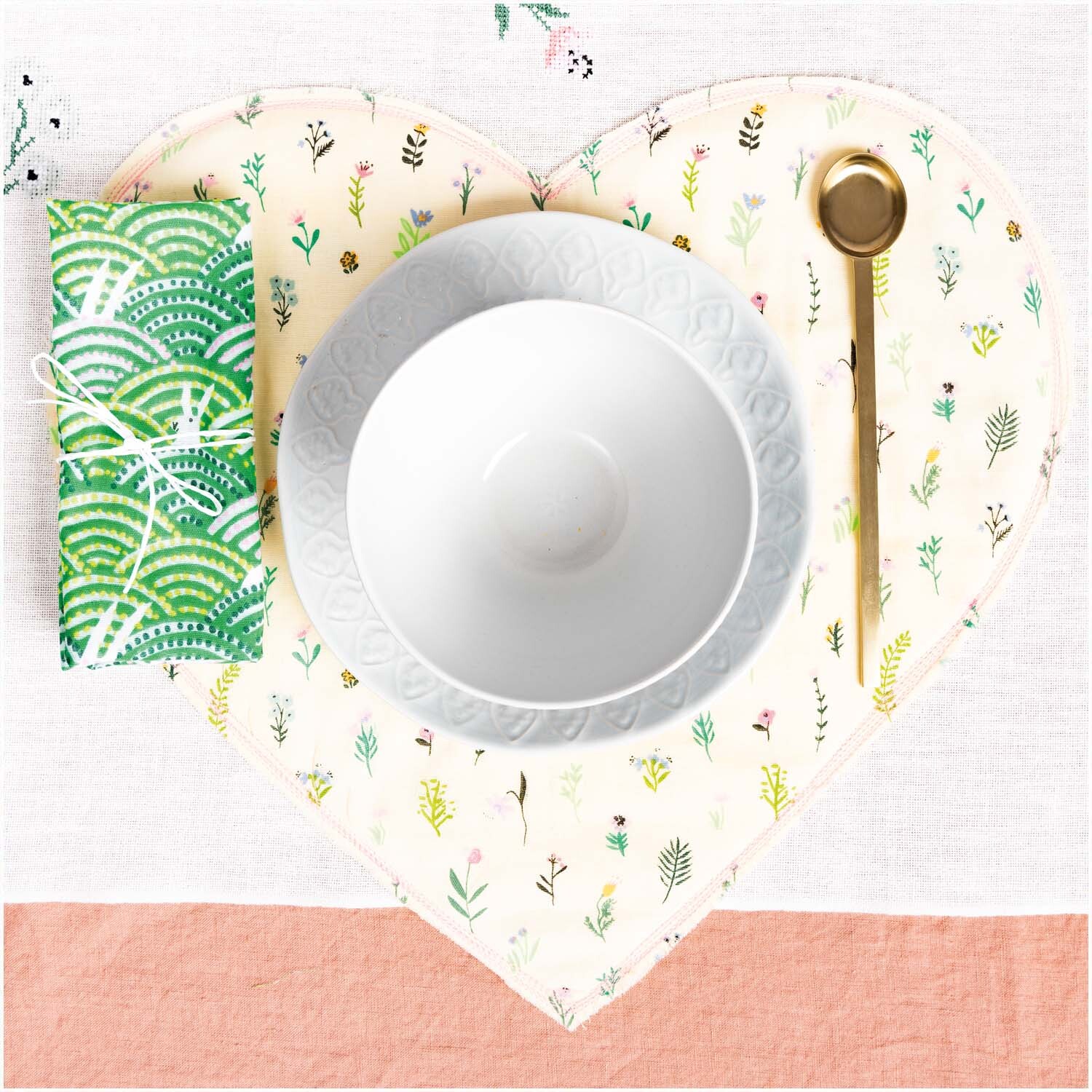 Musselin-Druckstoff Bunny Hop Streublumen zeigt eine Tischdekoration mit Herzuntersetzer, Schale und goldenem Löffel. Ideal für kreative Nähprojekte.
