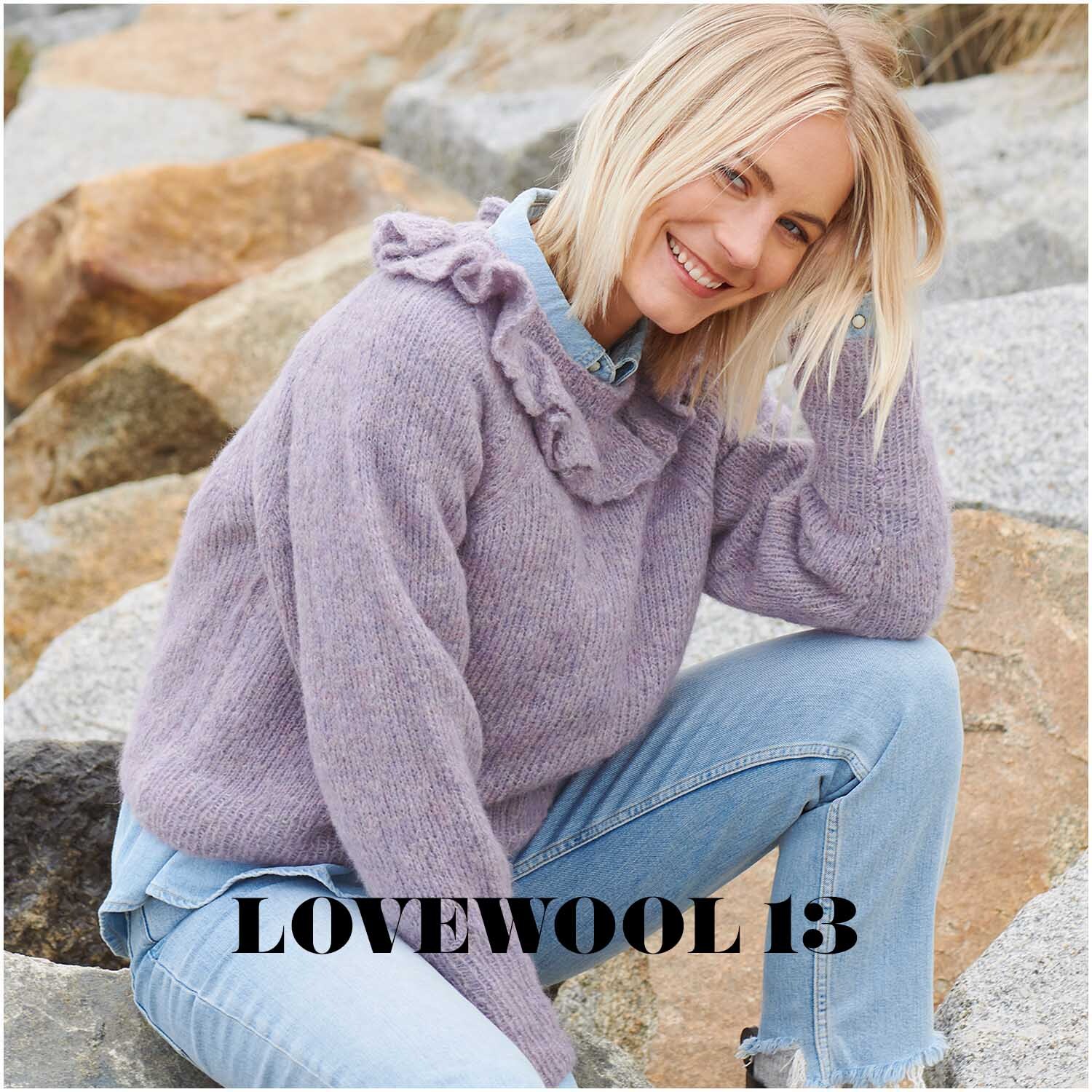 Fashion Skinny Alpaca aran: Frau in fliederfarbenem Pullover aus Alpaka-Wolle sitzt lächelnd auf Felsen.
