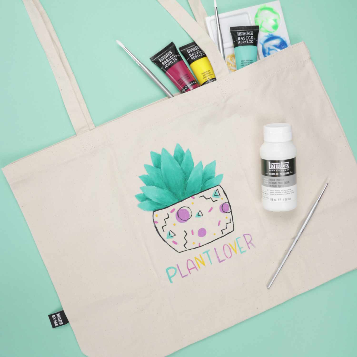 Anleitung Textilbeutel mit Acrylfarbe bemalen: Ein bemalter Beutel mit Pflanzenmotiv und Acrylfarben auf grünem Hintergrund.