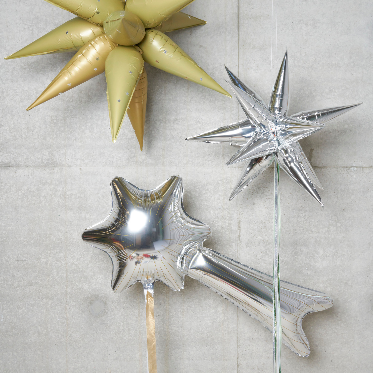 Folienballon Sternschnuppe 110x60cm in Silber von Rico Design, dekorativ neben einem goldenen Sternballon.