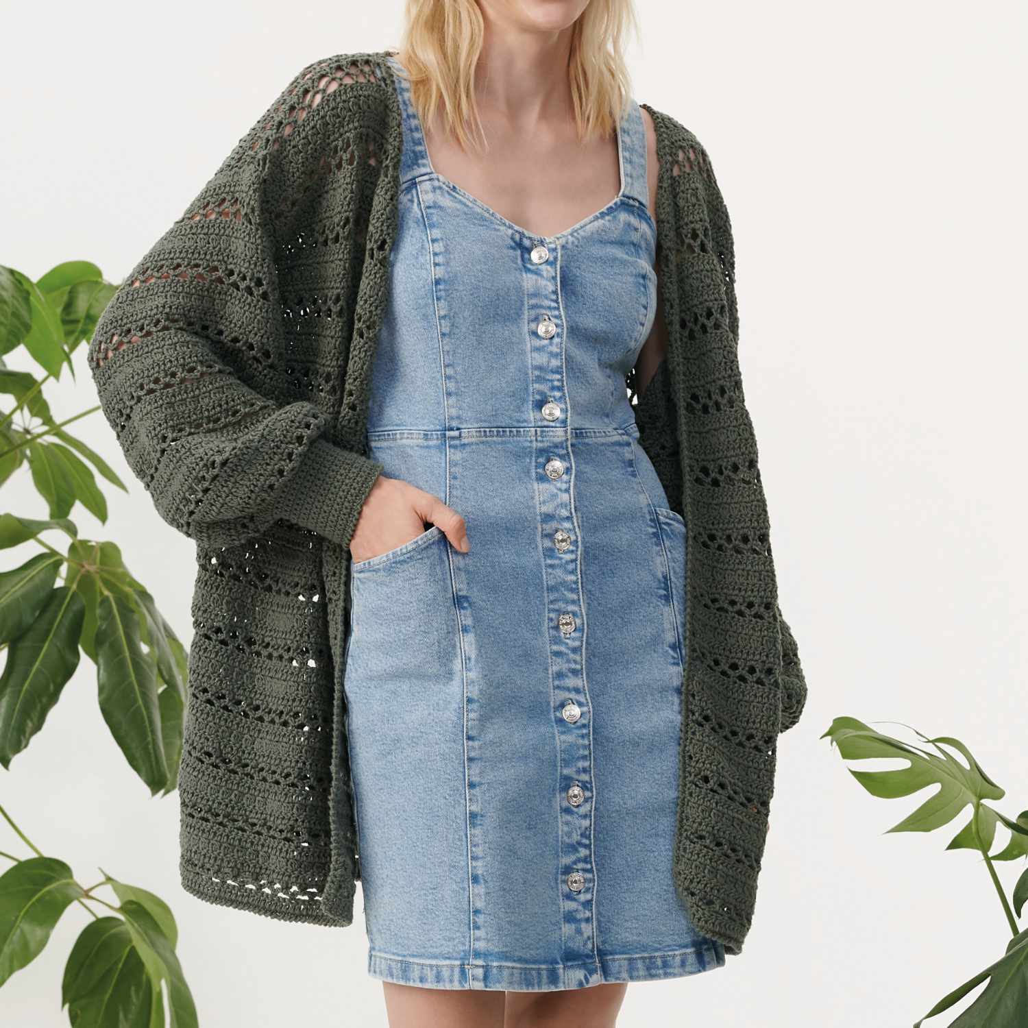 Häkelanleitung Cardigan aus Creative Sport dk: Frau trägt gestrickten Cardigan über Jeanskleid, umgeben von Pflanzen.