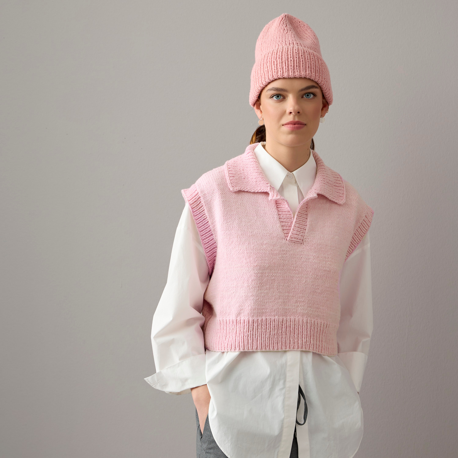 Essentials Vegan Cashmere aran: Frau trägt altrosa Pullunder und Mütze über weißer Bluse.