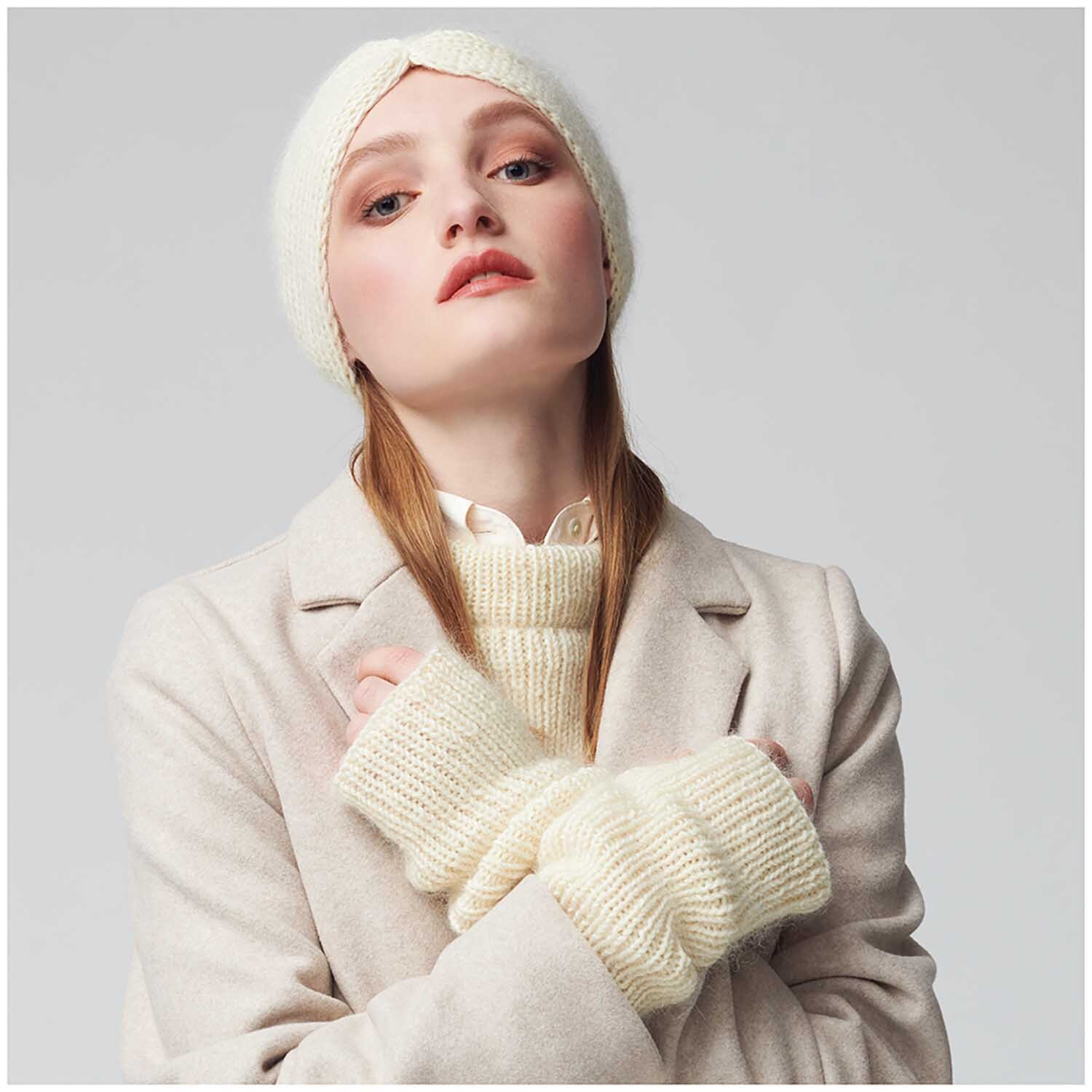 Essentials Merino dk: Frau in cremefarbenem Mantel mit passender Mütze und Handschuhen aus Rico Design Wolle.