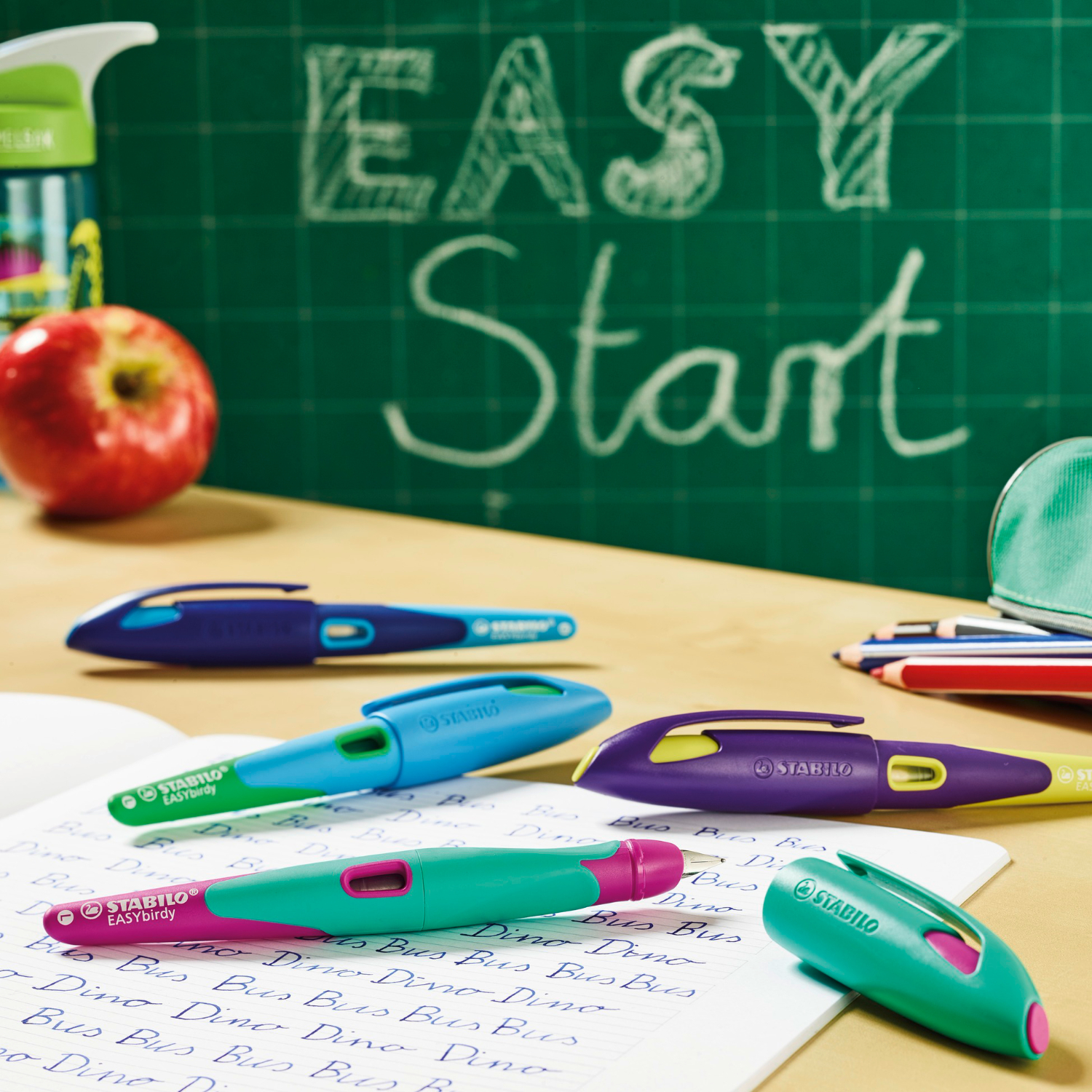 Easybird Patronenfüller für Linkshänder auf einem Schreibtisch mit Schulmaterialien und Tafel im Hintergrund.