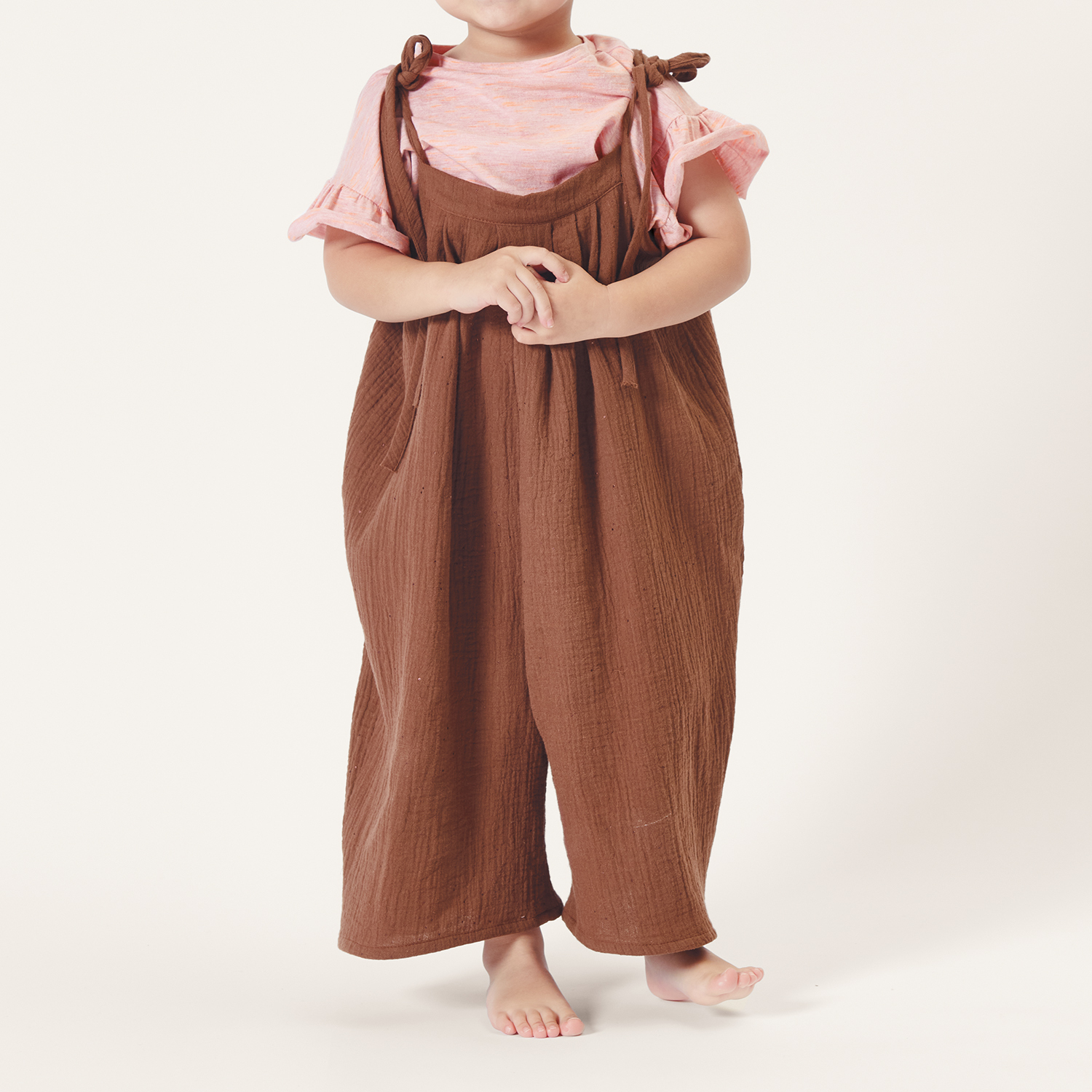 Nähanleitung Latzhose aus Krinkelmusselin: Kind trägt braune Latzhose und rosa Oberteil.