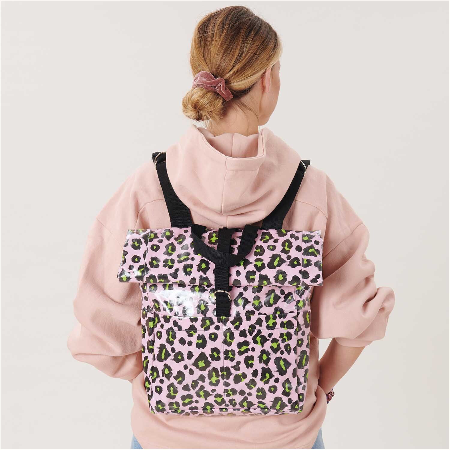 Stoffabschnitt PVC-Stoff Glossy Acid Leo rosa 25x70cm: Frau mit rosa Hoodie trägt Rucksack aus glänzendem Leopardenmuster-Stoff.