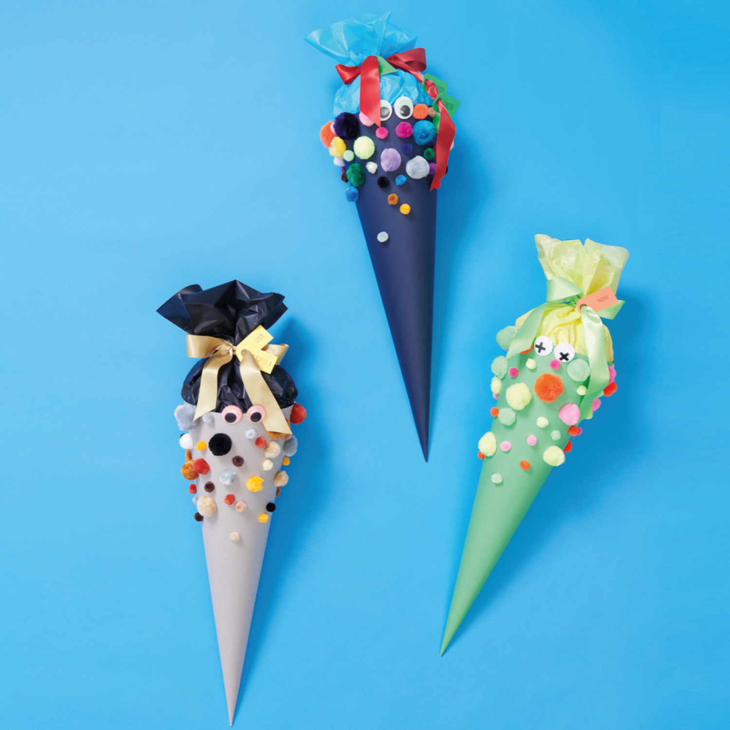 Bastelanleitung Schultüte mit bunten Wackelaugen und Pompons auf blauem Hintergrund.