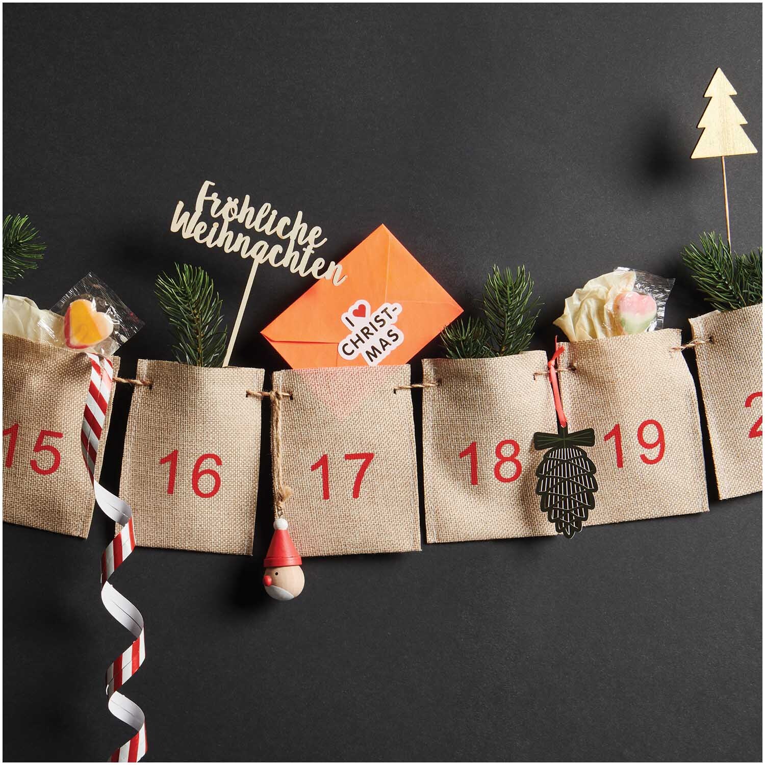 Adventskalender Girlande 1-24 260cm mit nummerierten Jutesäckchen, dekoriert mit Tannenzweigen und Weihnachtsornamenten.