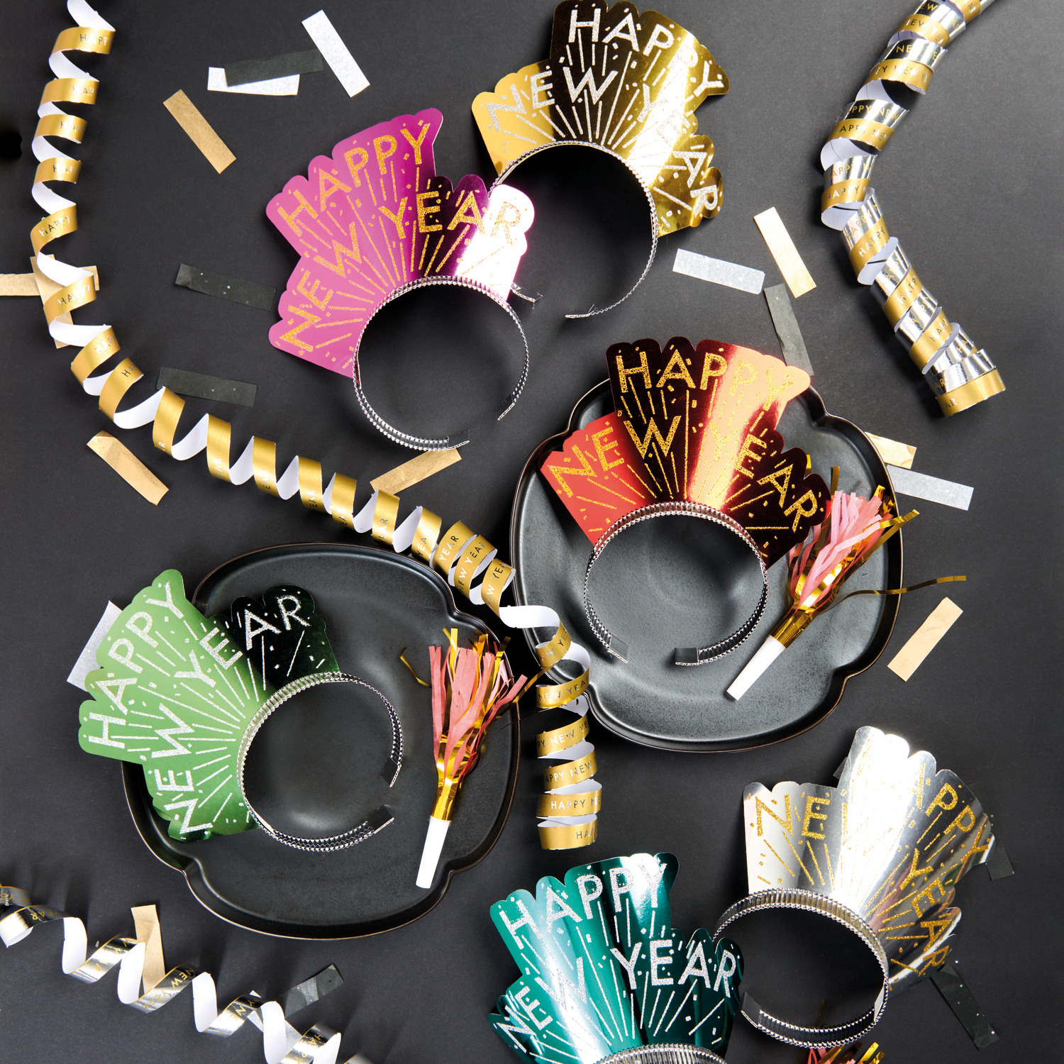Haarreifen Happy New Year 6 Stück von Rico Design in verschiedenen Farben auf schwarzem Hintergrund, umgeben von goldenen und silbernen Partydekorationen.