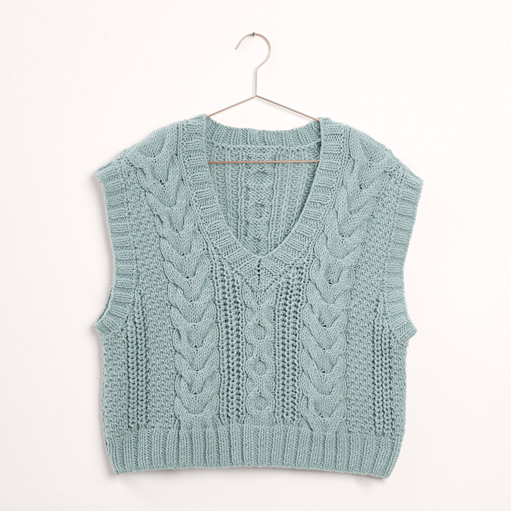 Blauer Pullunder mit Zopfmuster auf grauem Hintergrund – zum Strickset