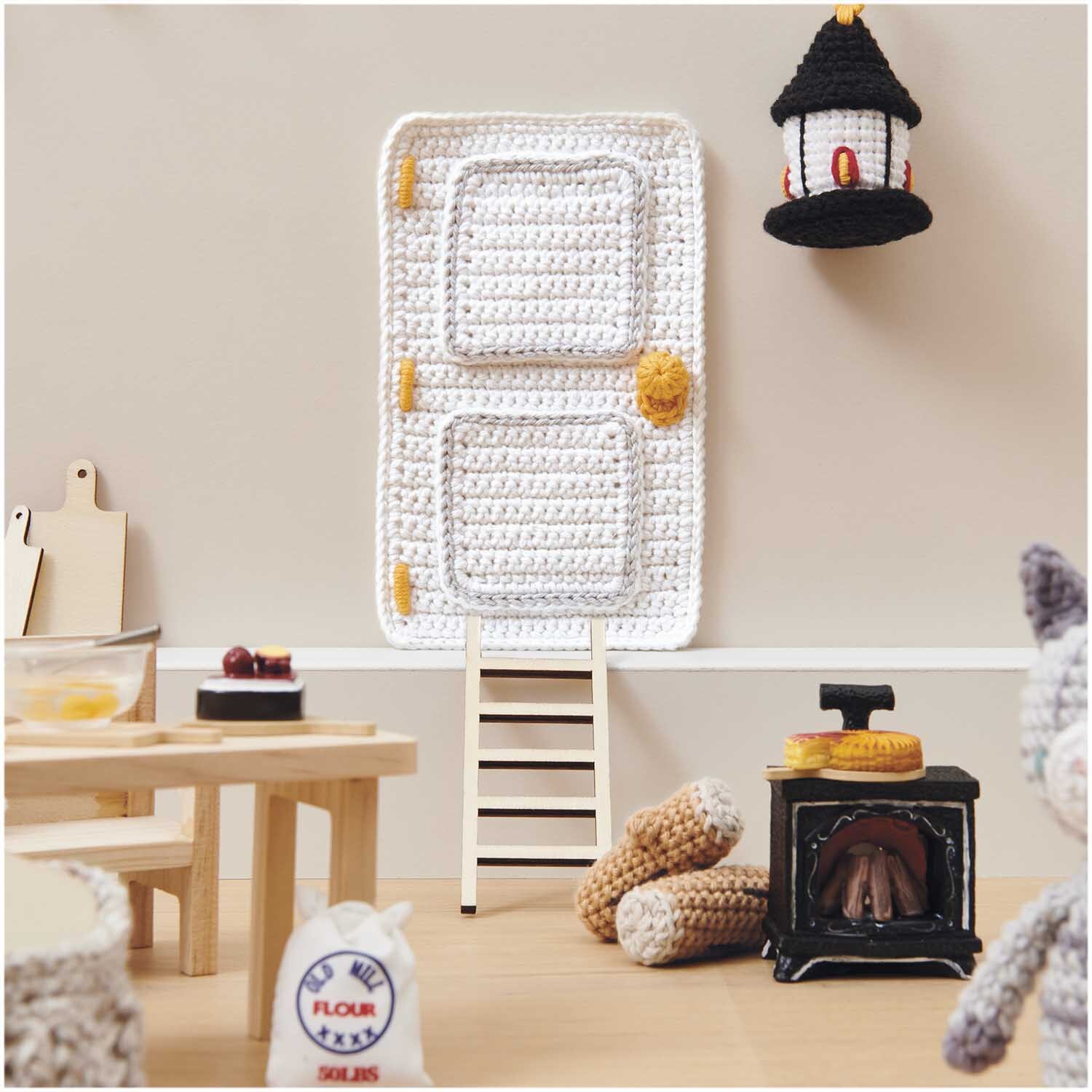 Miniatur Kamin mit Licht in einer gemütlichen Puppenhausküche, umgeben von gehäkelten Accessoires.