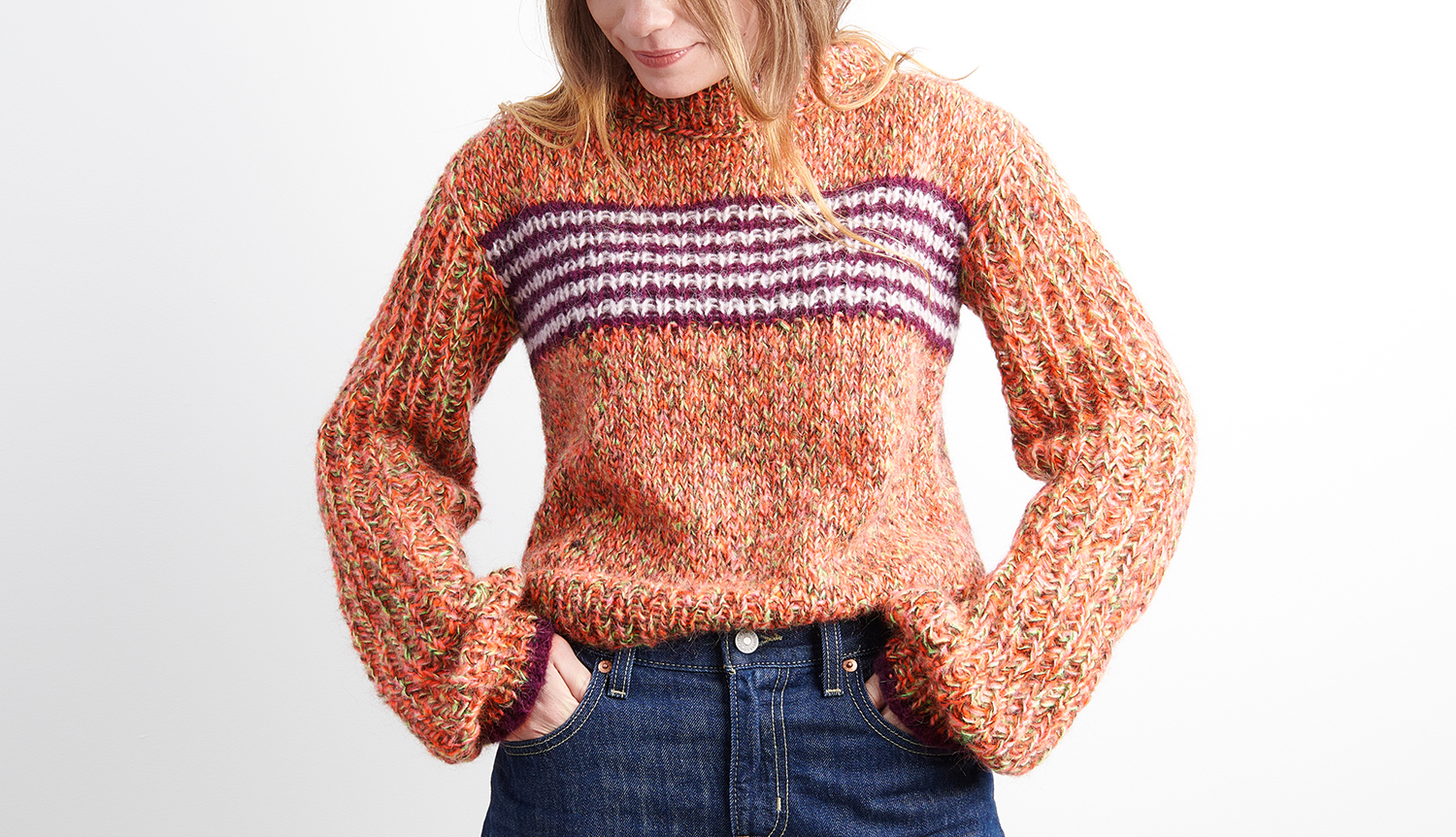 Strickanleitung Pullover mit coolem Print: Frau trägt orangefarbenen Pullover mit lila Streifenmuster.
