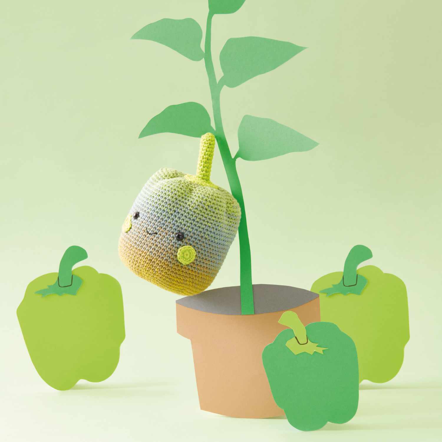 Häkelset Paprika aus Ricorumi Fresh Friends: Eine gehäkelte Paprika an einem grünen Stängel in einem Topf, umgeben von drei grünen Paprika.