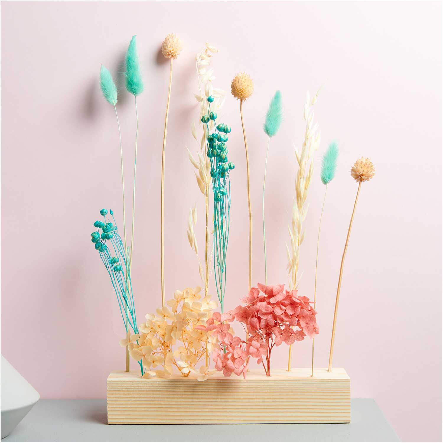 Getrockneter Flachs türkis 60-75cm 100g von Rico Design in einem Holzständer arrangiert vor rosa Hintergrund.