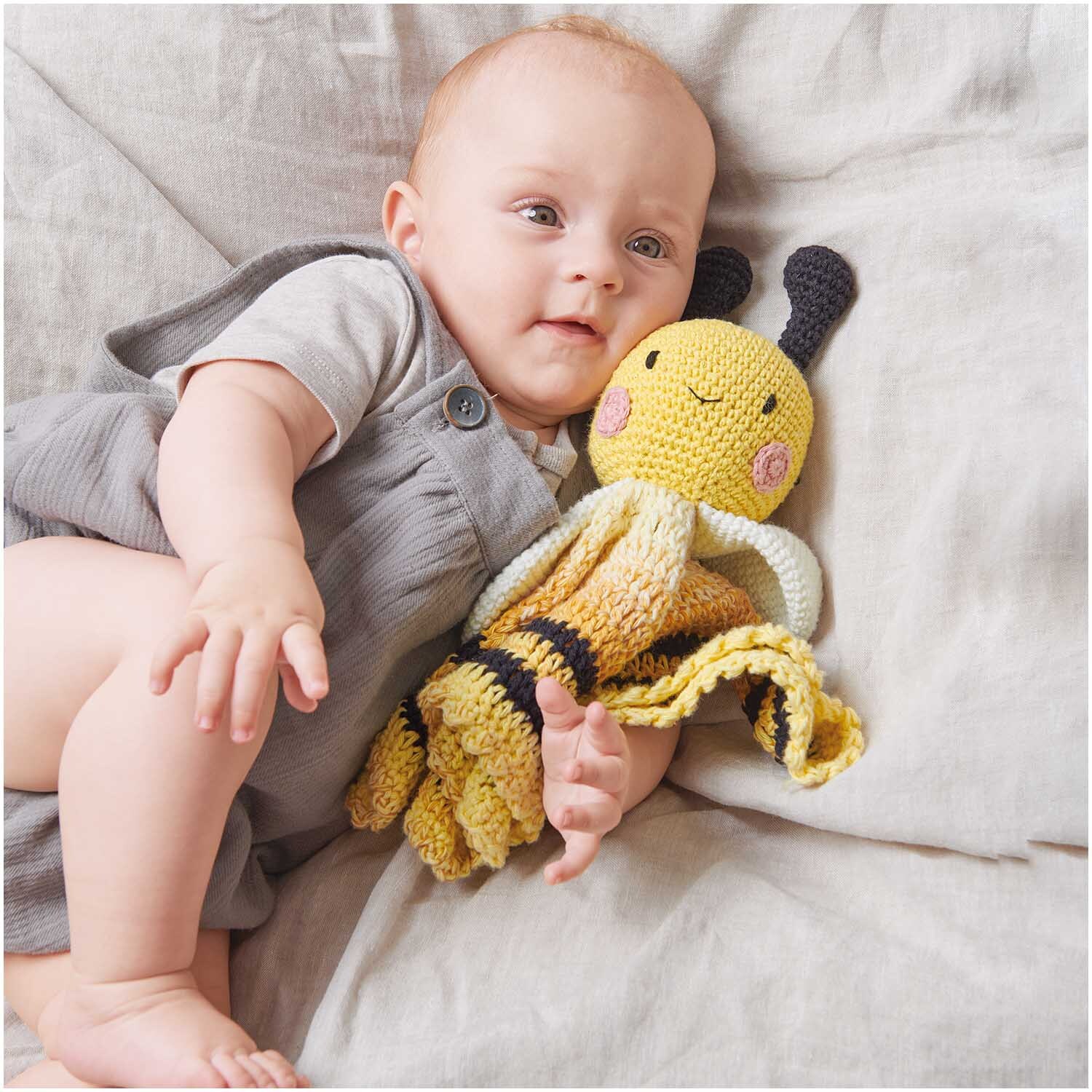 Häkelset Ricorumi Baby Blankies Biene: Ein Baby kuschelt mit einer gelben, gehäkelten Biene.