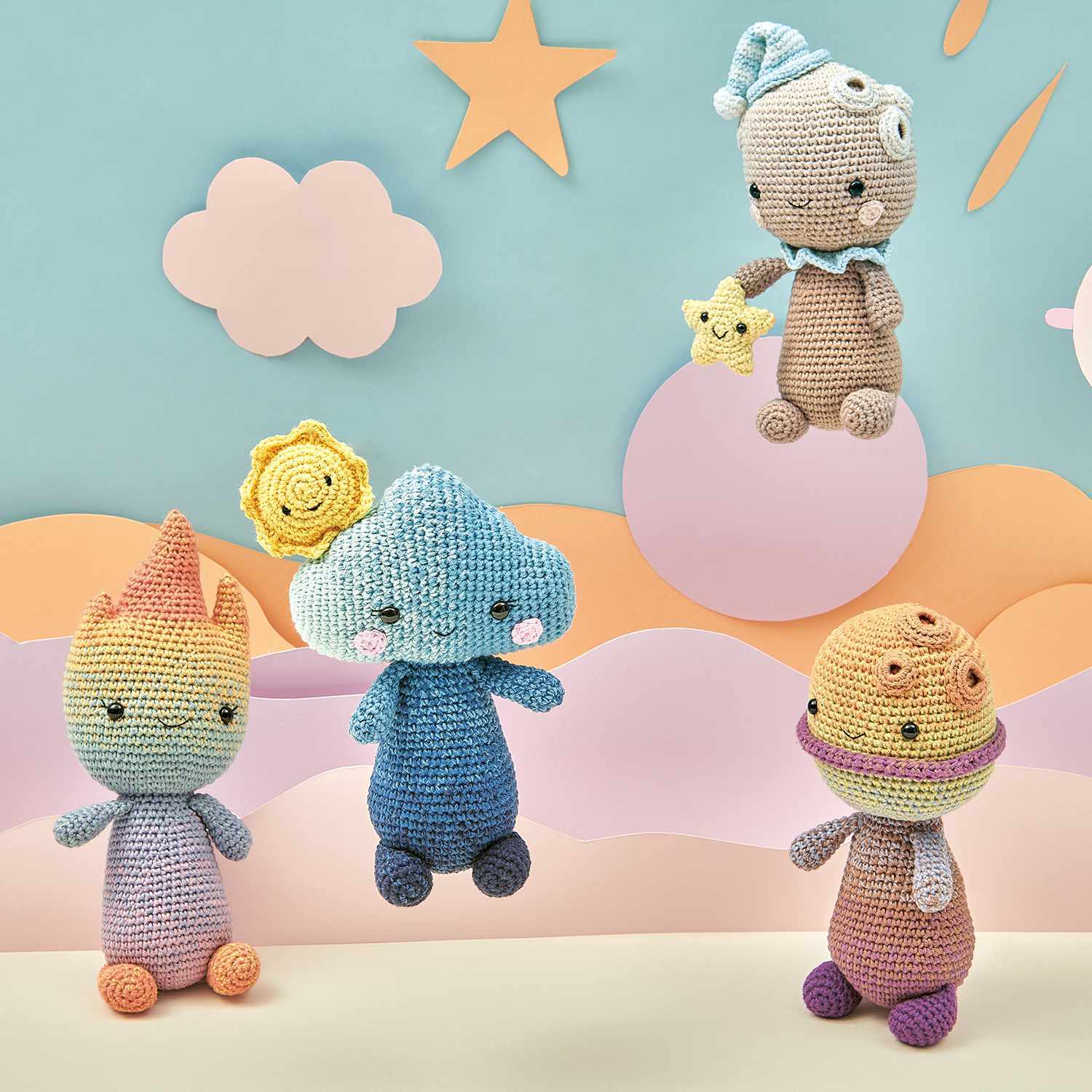 Häkelset Planet-Head aus Ricorumi Element Heads: Vier bunte, gehäkelte Figuren vor einem pastellfarbenen Hintergrund mit Wolken und Sternen.
