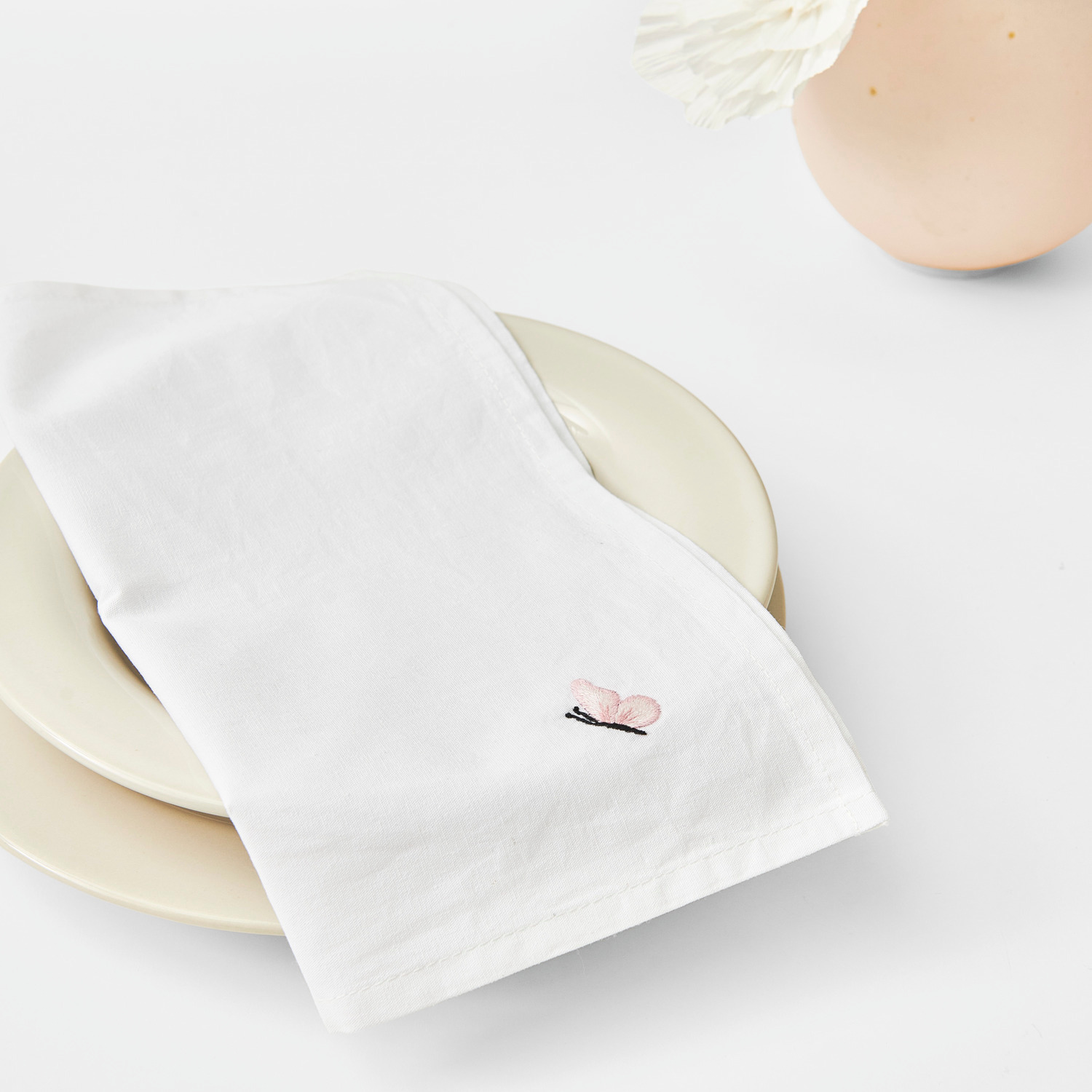 Stoffserviette 2 Stück weiß von Rico Design auf einem Teller, elegant gefaltet mit zartem Muster.