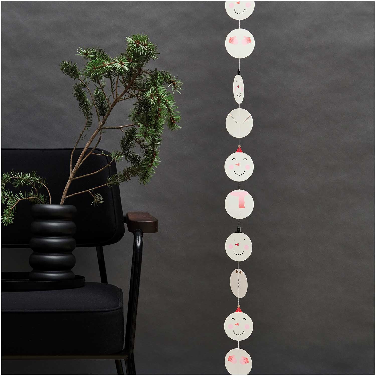 Paper Poetry Genähte Girlande Schneemänner 2,3m: Weiße Schneemann-Girlande von Rico Design, dekorativ an schwarzem Stuhl und Pflanze.