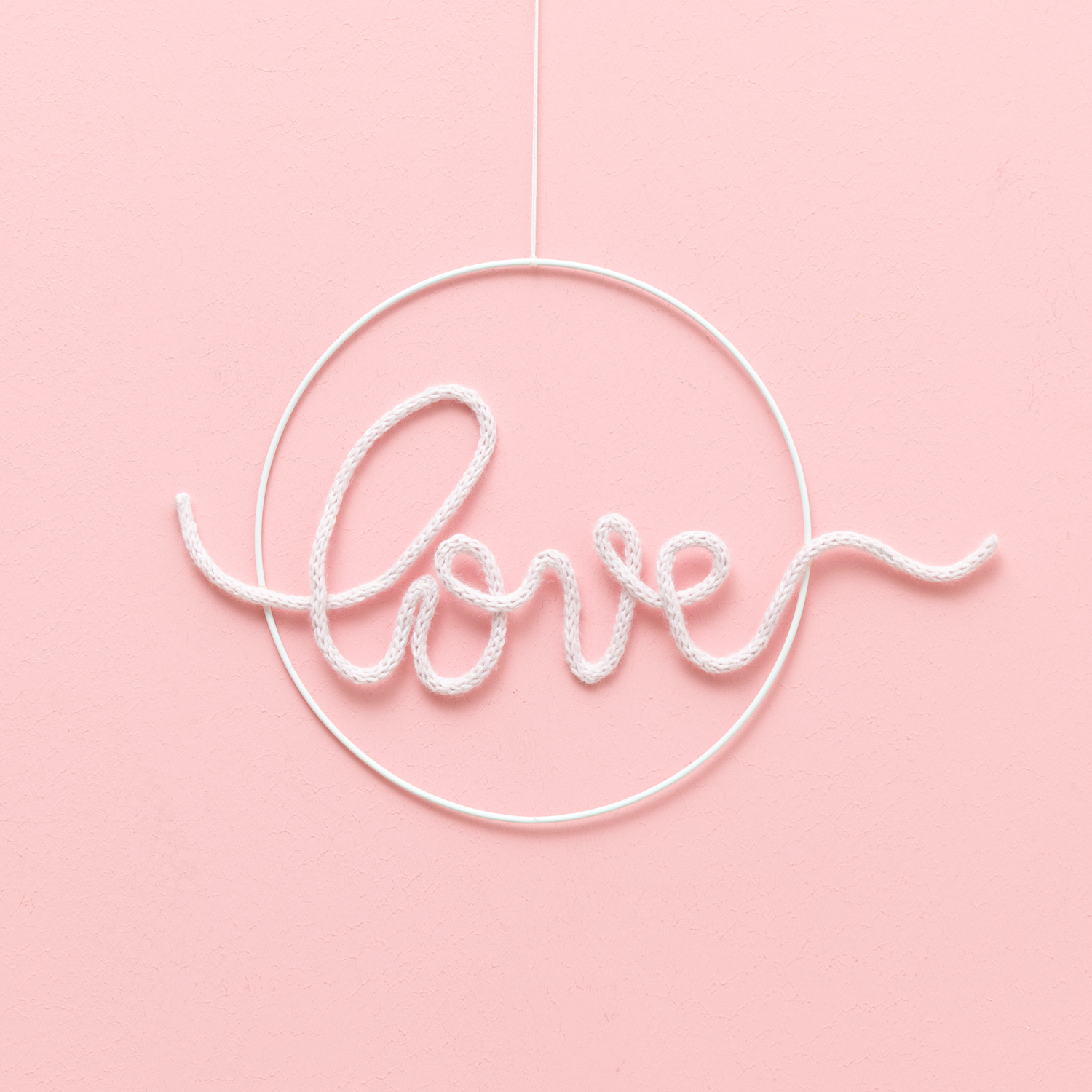 Bastelanleitung Wanddeko mit Strickschläuchen: Weißer Schriftzug "love" in Kreisform auf rosa Hintergrund.