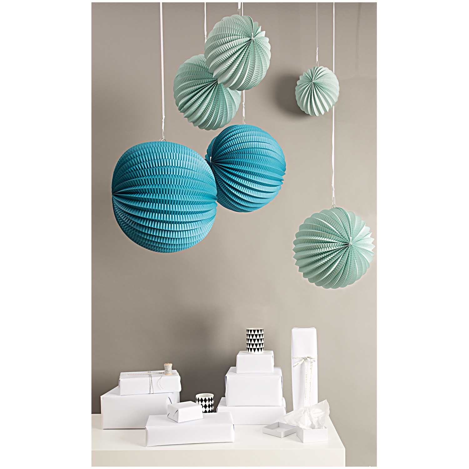 Lampions aqua 3 Stück von Rico Design schweben über einem Tisch mit weißen Geschenkboxen.