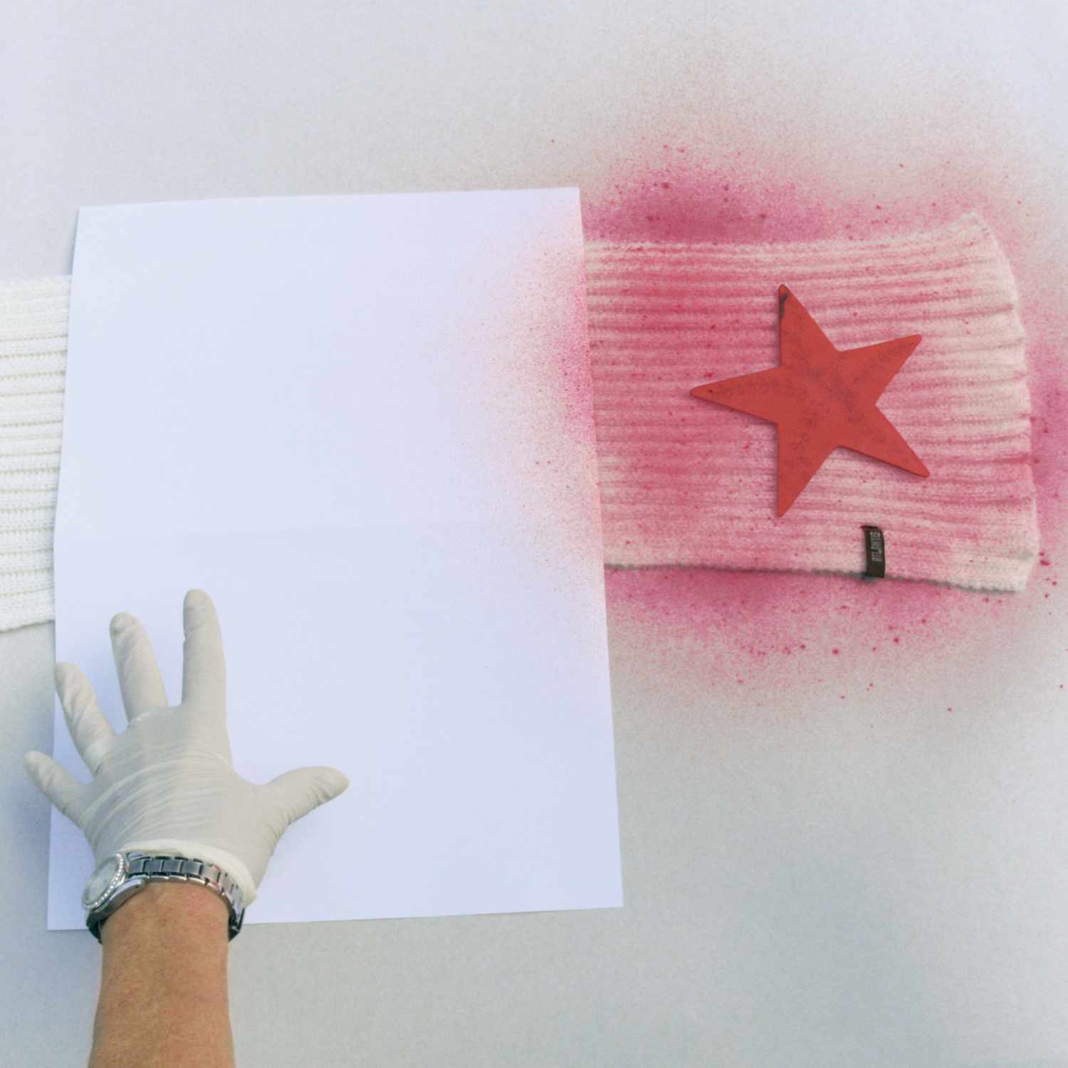 Fashion Spray: Kreatives Design mit pinkem Stern auf weißem Stoff, Hand mit Handschuh hält Papier.