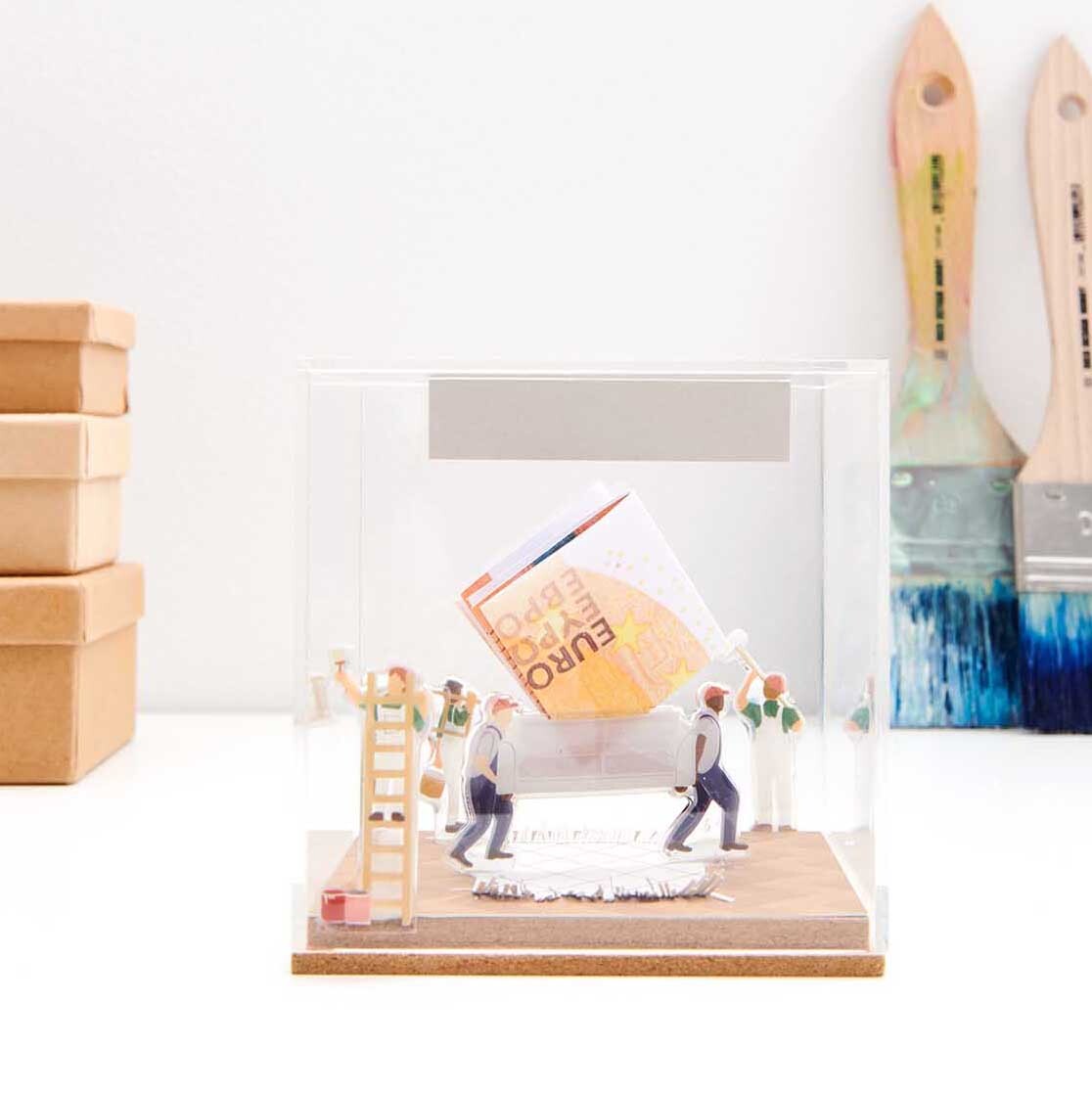 Figurico Gelsticker Umzug: Miniatur-Szene mit Figuren, die einen Karton tragen. Hintergrund mit Pinseln.