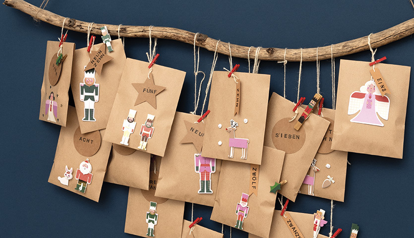 Bastelanleitung Last Minute Adventskalender aus Flachbeuteln an einem Ast, dekoriert mit bunten Figuren und Klammern, ideal für kreative Weihnachtsvorbereitungen.