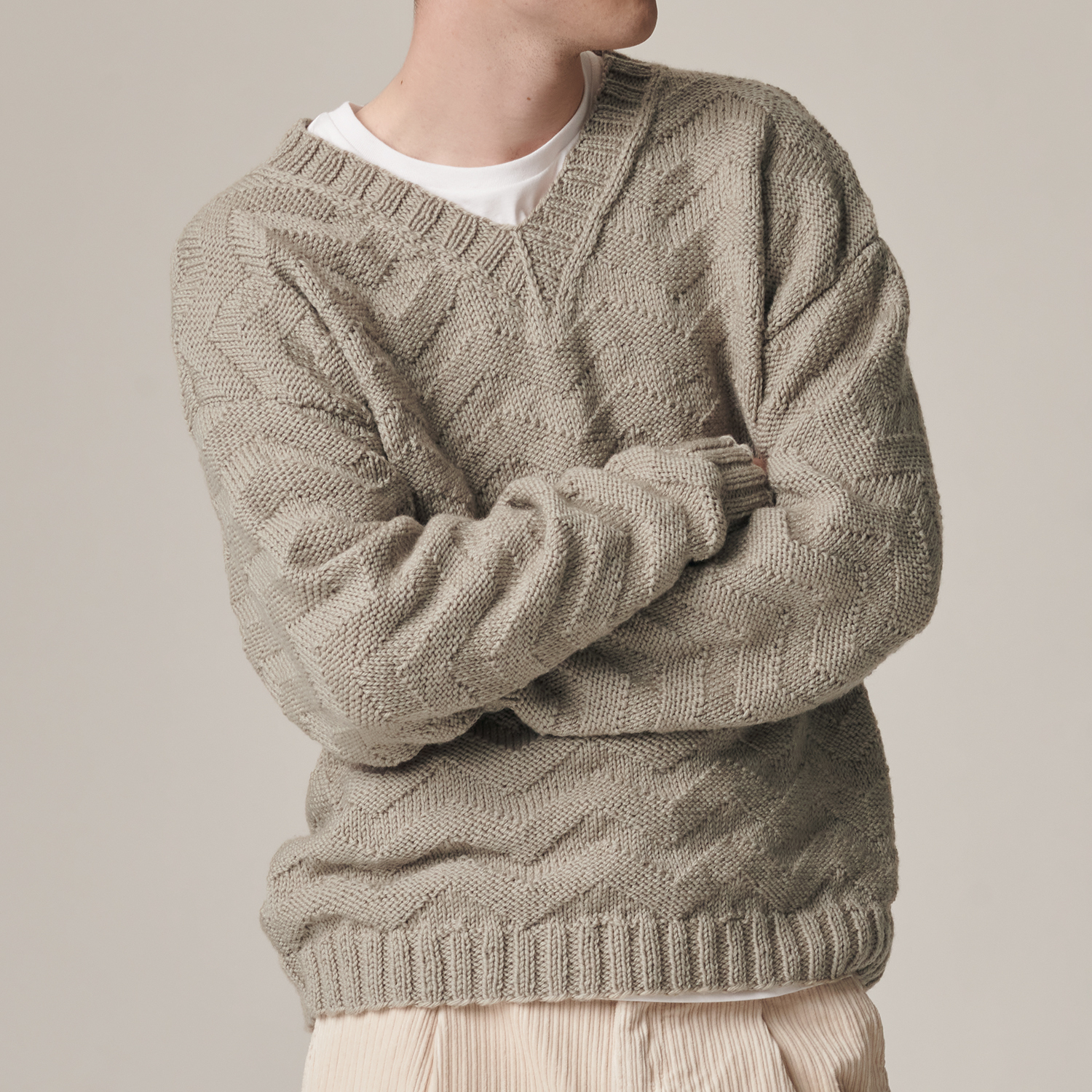Strickanleitung Pullover aus Essentials Soft Merino aran: Mann trägt beigefarbenen Strickpullover mit V-Ausschnitt, kombiniert mit heller Hose.