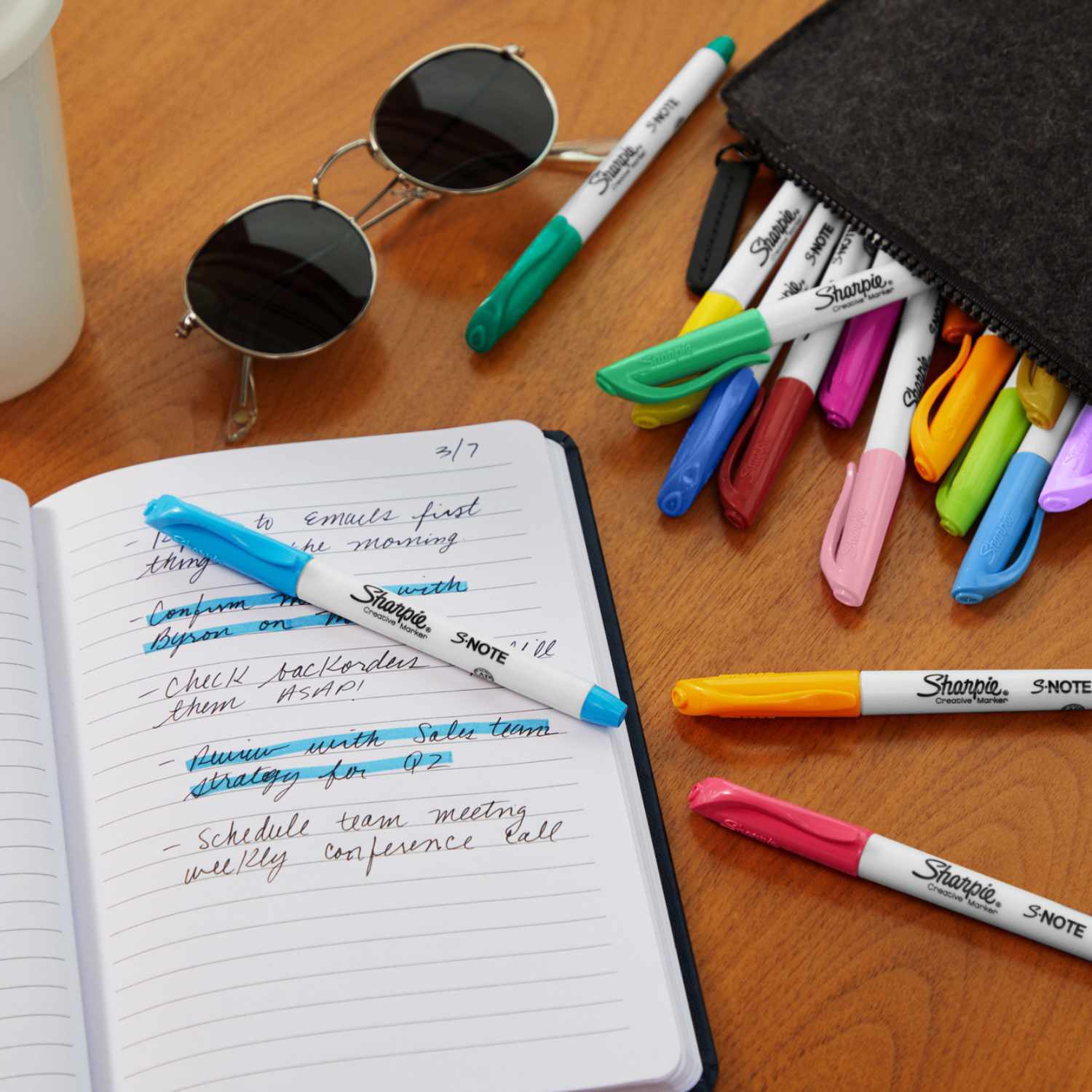 Marker S-Note 12 Stück: Bunte Sharpie-Marker auf einem Tisch neben einem Notizbuch und Sonnenbrille.