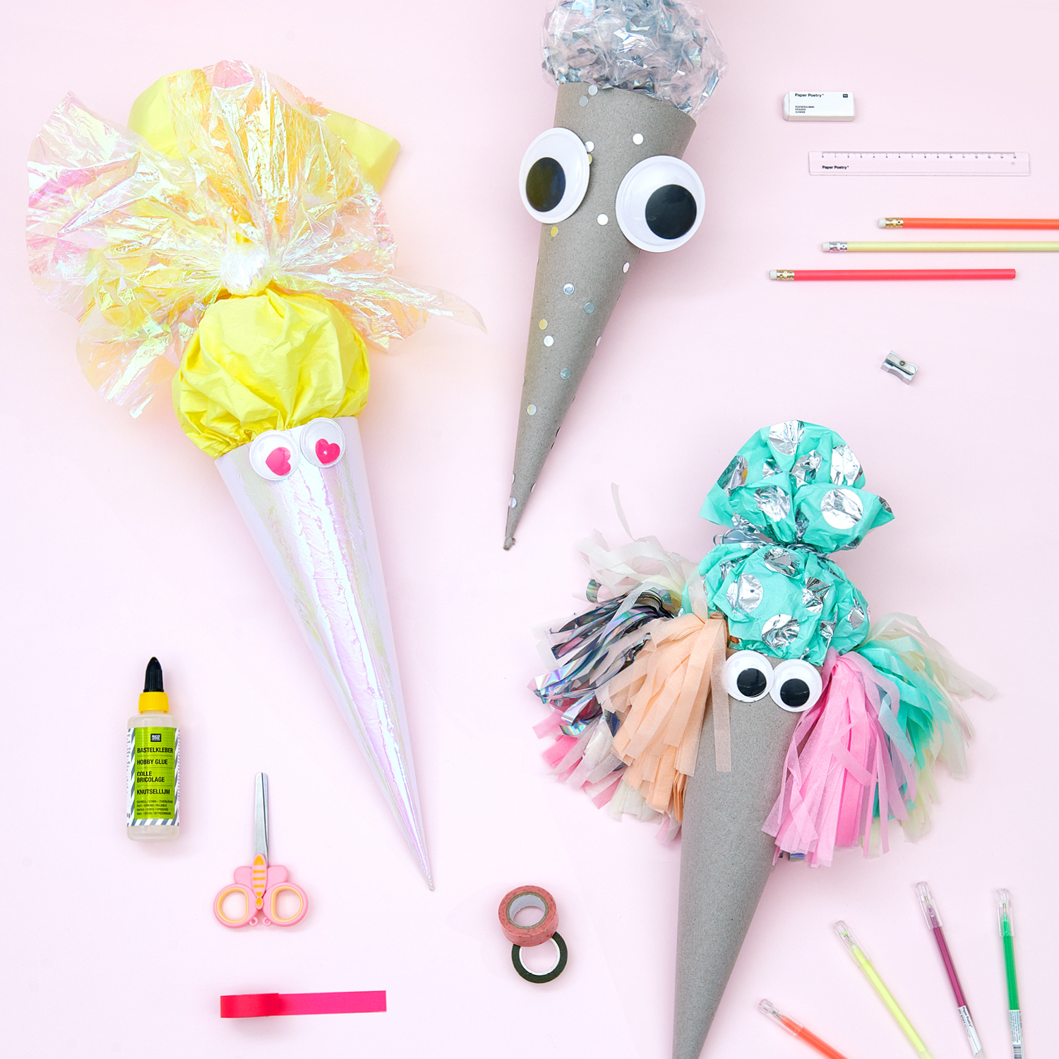 Bastelanleitung Geschwister-Schultüten mit Wackelaugen: Drei bunte Schultüten mit Wackelaugen und Bastelmaterialien auf rosa Hintergrund.
