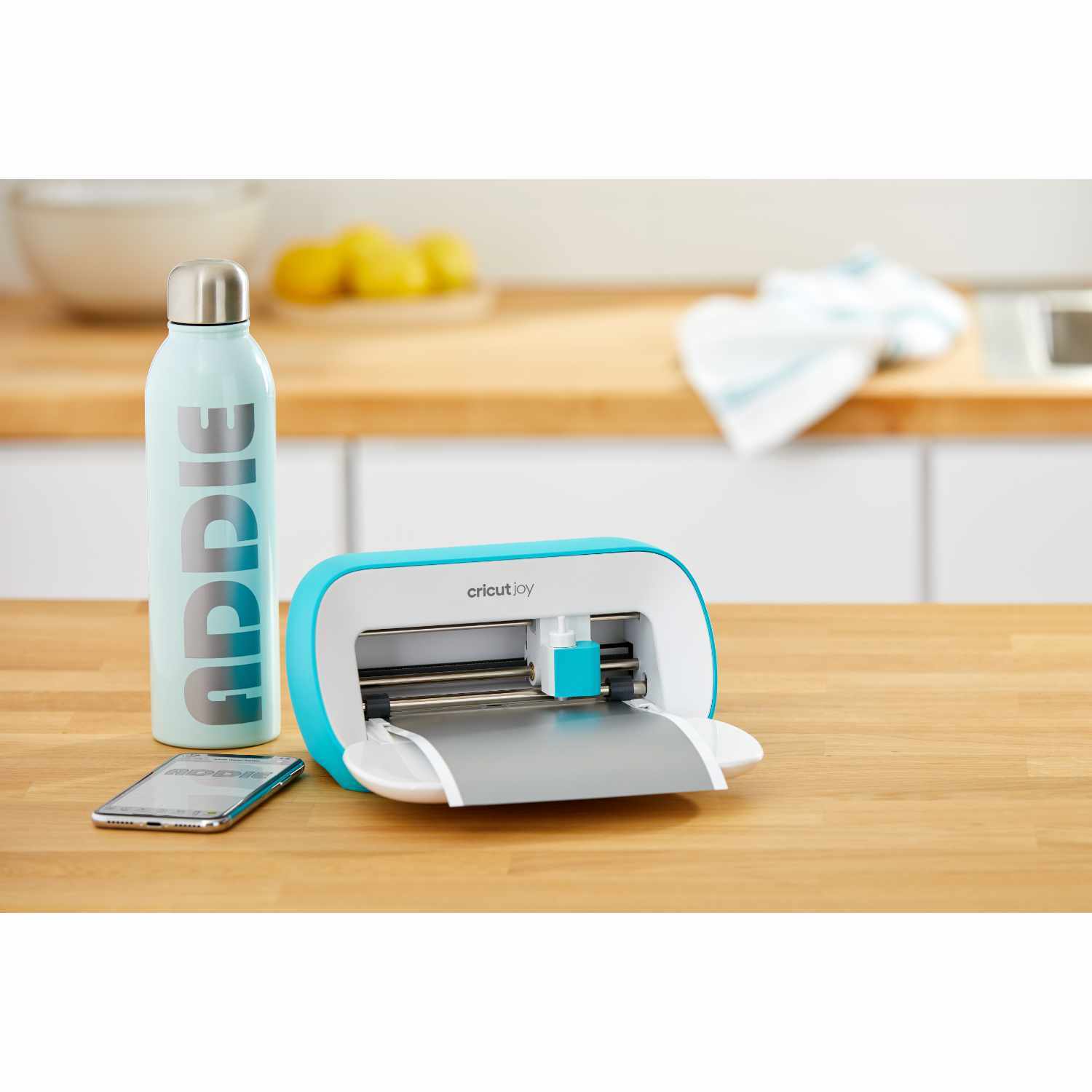 Joy Schneideplotter von Cricut auf einem Tisch, neben einer Wasserflasche und einem Smartphone. Ideal für kreative Projekte.