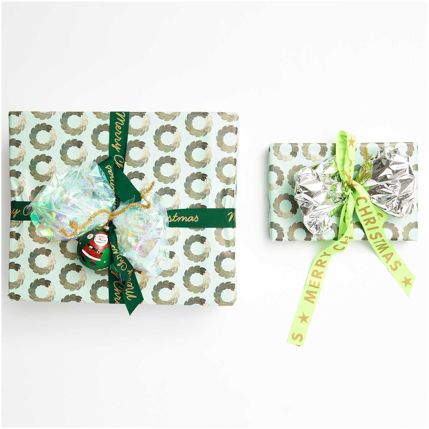Paper Poetry Geschenkpapier mit Kränzen, dekoriert mit grünen Schleifen und weihnachtlichen Motiven.