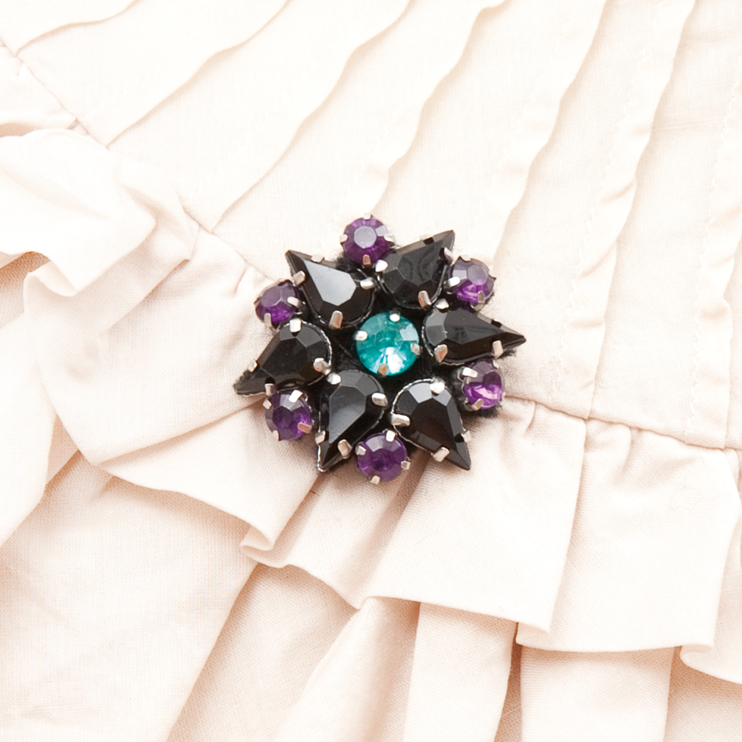 Anleitung Dekorative Brosche basteln: Elegante Brosche mit schwarzen und violetten Steinen auf beigem Stoff.