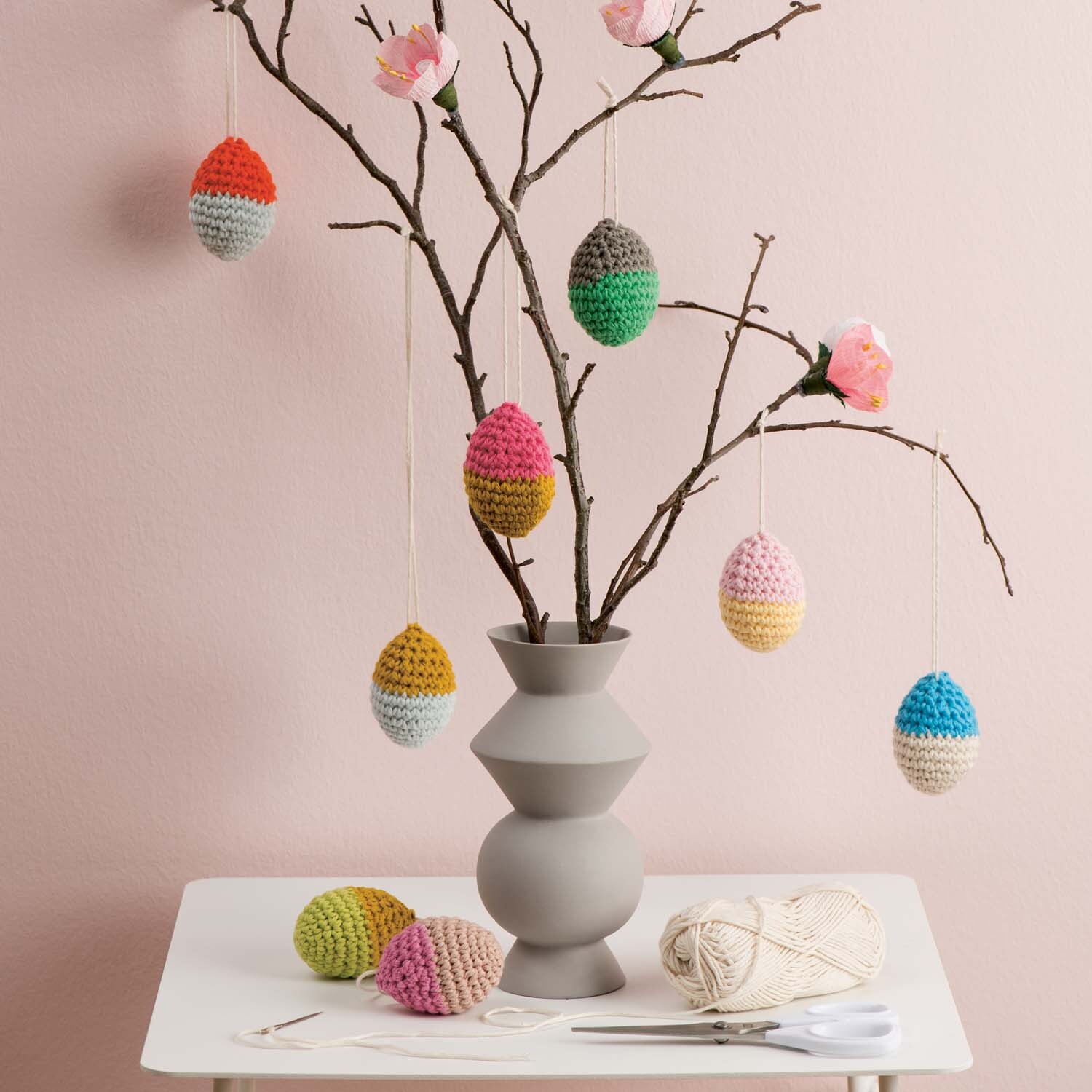 Häkelanleitung Ostereier: Bunter Osterstrauß mit gehäkelten Eiern in Vase auf weißem Tisch.