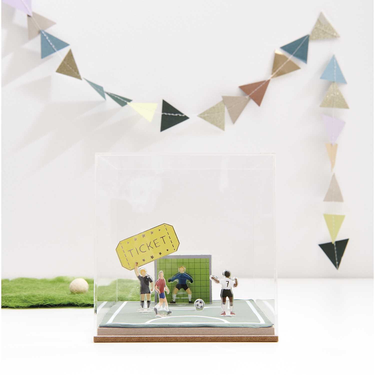 Figurico Gelsticker Fußballspieler: Miniatur-Fußballszene in Vitrine, dekoriert mit bunten Wimpeln.