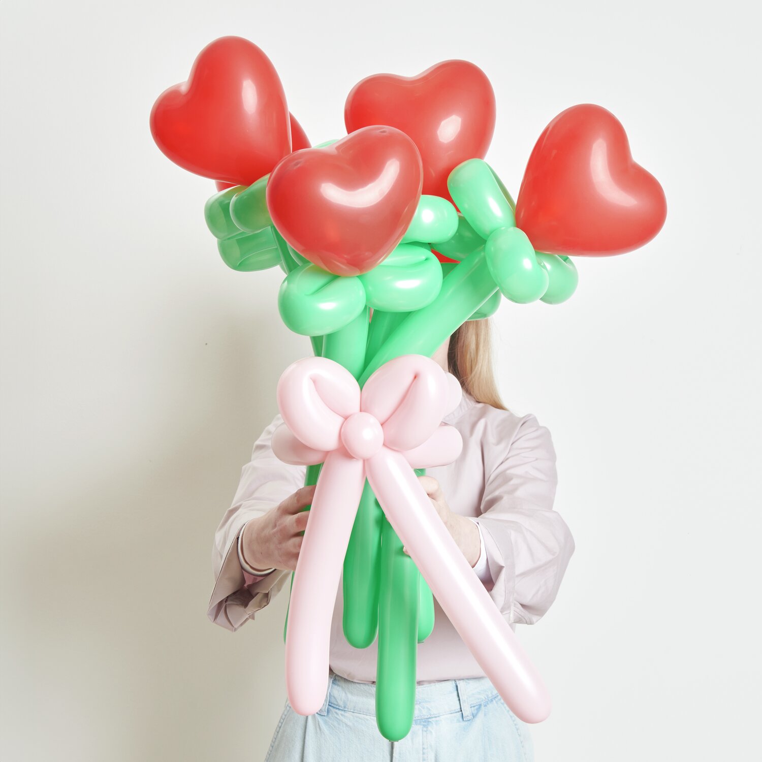 Ballonstrauß Herzen Rot: Frau hält Strauß aus roten Herzballons mit grünen Stielen und rosa Schleife.