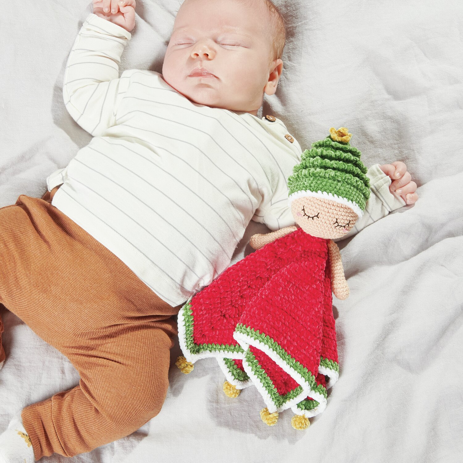 Ricorumi Baby Blankies Nilli Nilli: Ein Baby schläft neben einer gehäkelten Puppe in Rot und Grün.