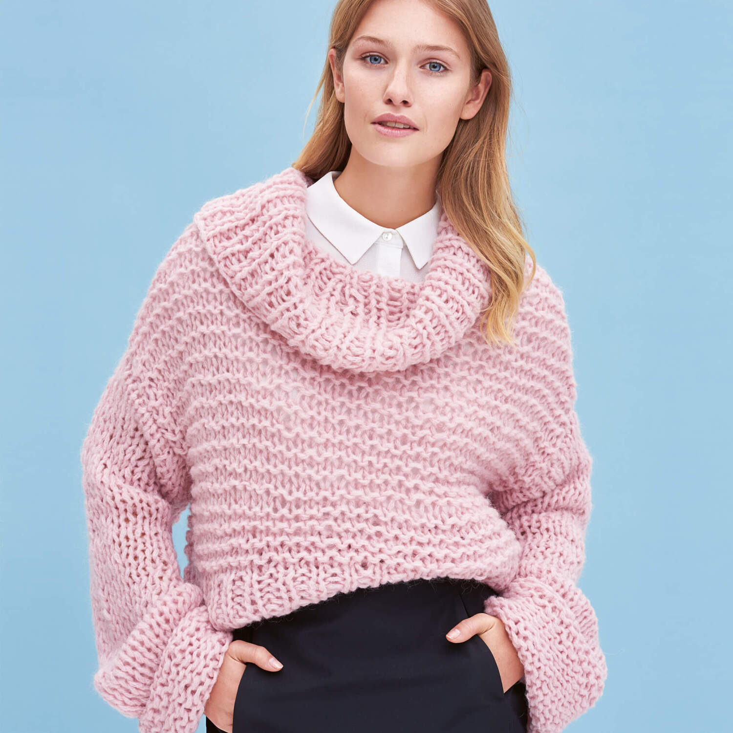 Strickanleitung Pullover aus Mohair Soft: Frau trägt einen rosa, grob gestrickten Pullover vor blauem Hintergrund.