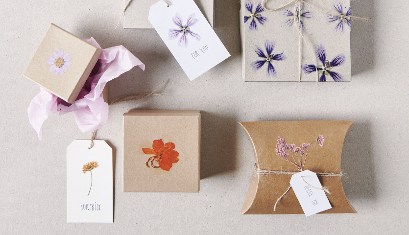 Bastelanleitung Karten und Schachteln mit gepressten Blumen: Verschiedene Boxen mit floralen Designs und Etiketten auf beigem Hintergrund.